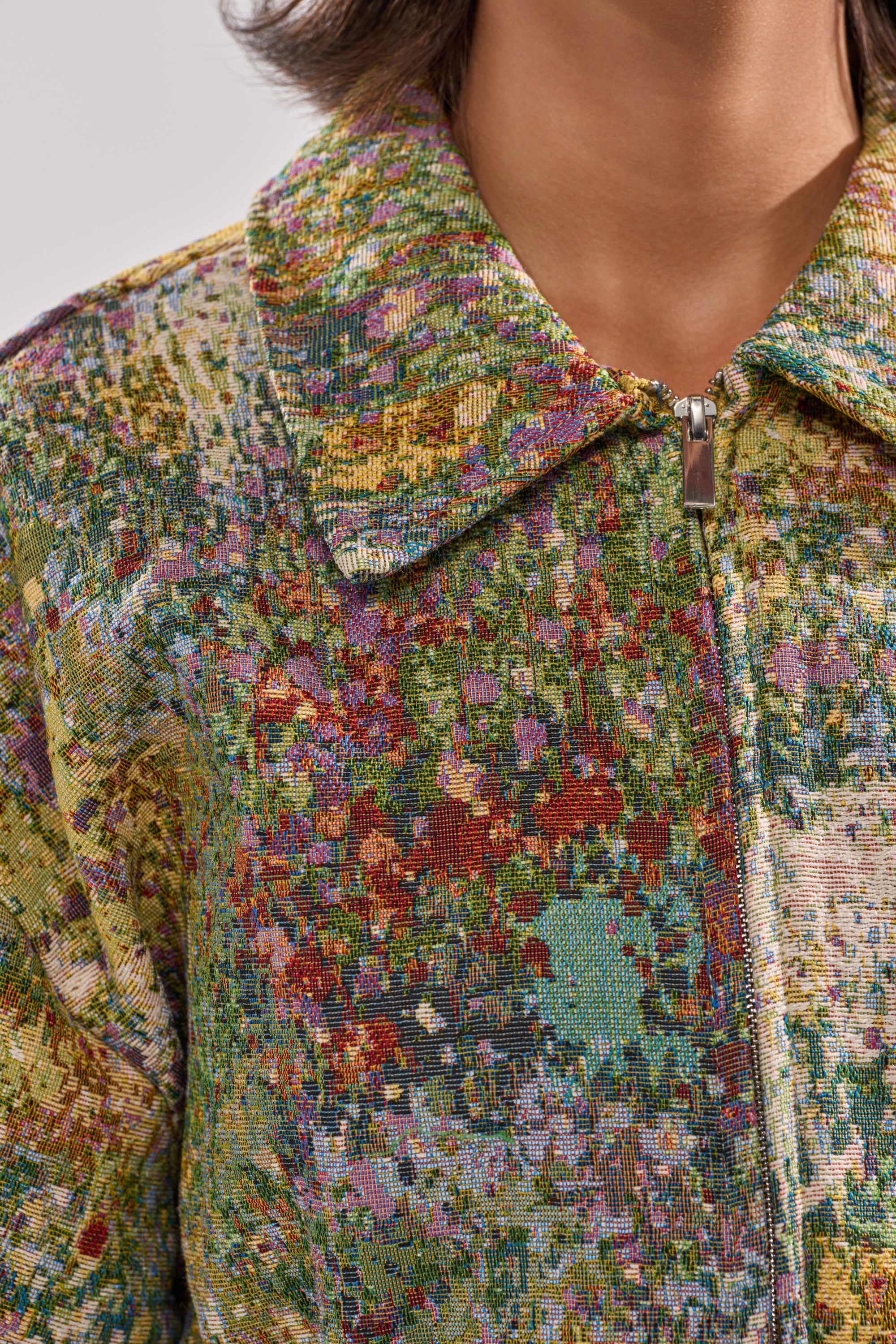 Close-up of a person wearing the DEEP IN THE SEA BROCADE BLOUSE, featuring a colorful, textured jacquard pattern, zipper closure, and pointed collar. The face is not visible.