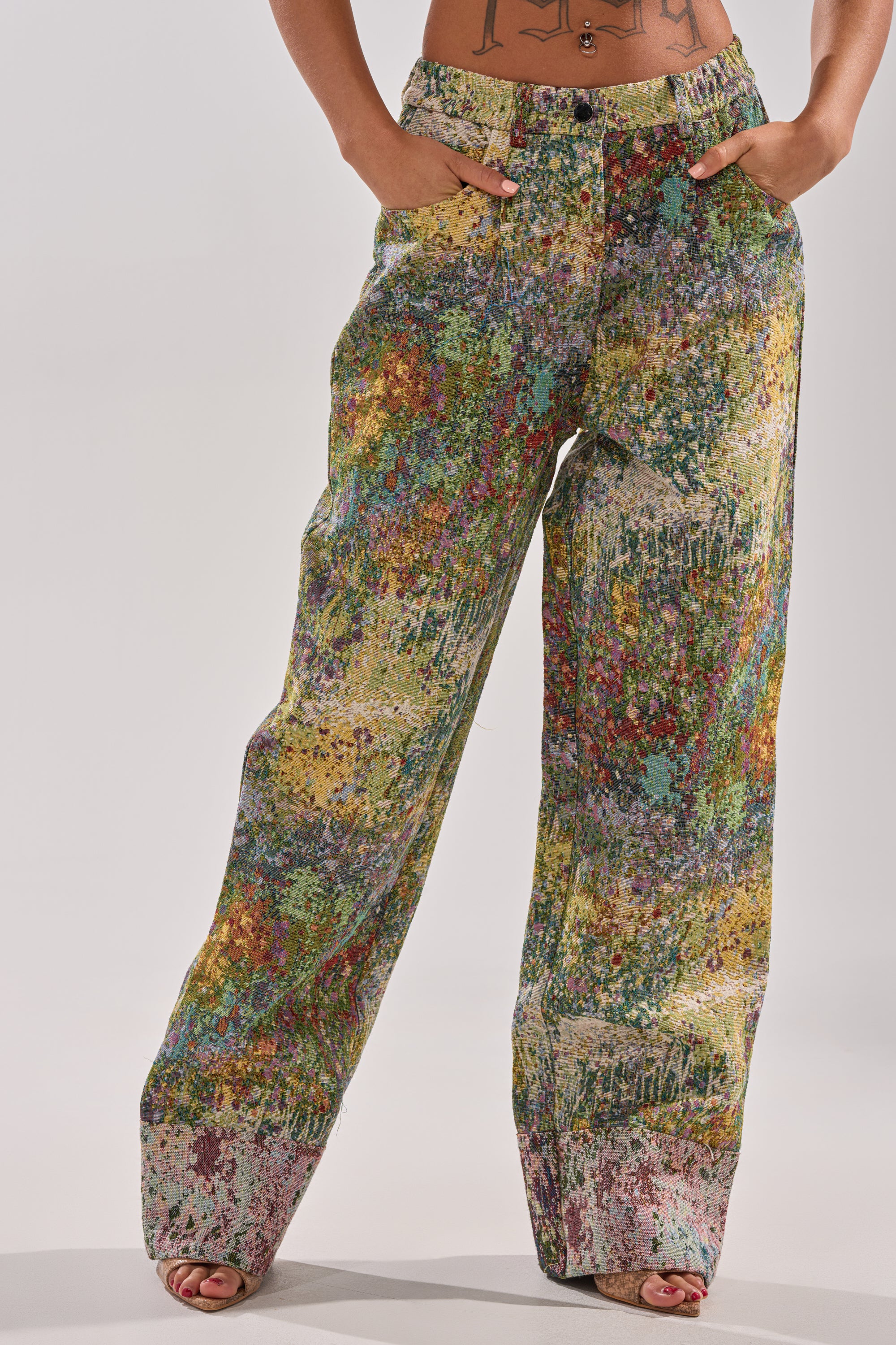 A person models the DEEP IN THE SEA BROCADE TROUSER, featuring a high-rise, wide-leg silhouette and vibrant abstract pattern. Only the lower torso and legs are visible against a plain light background.