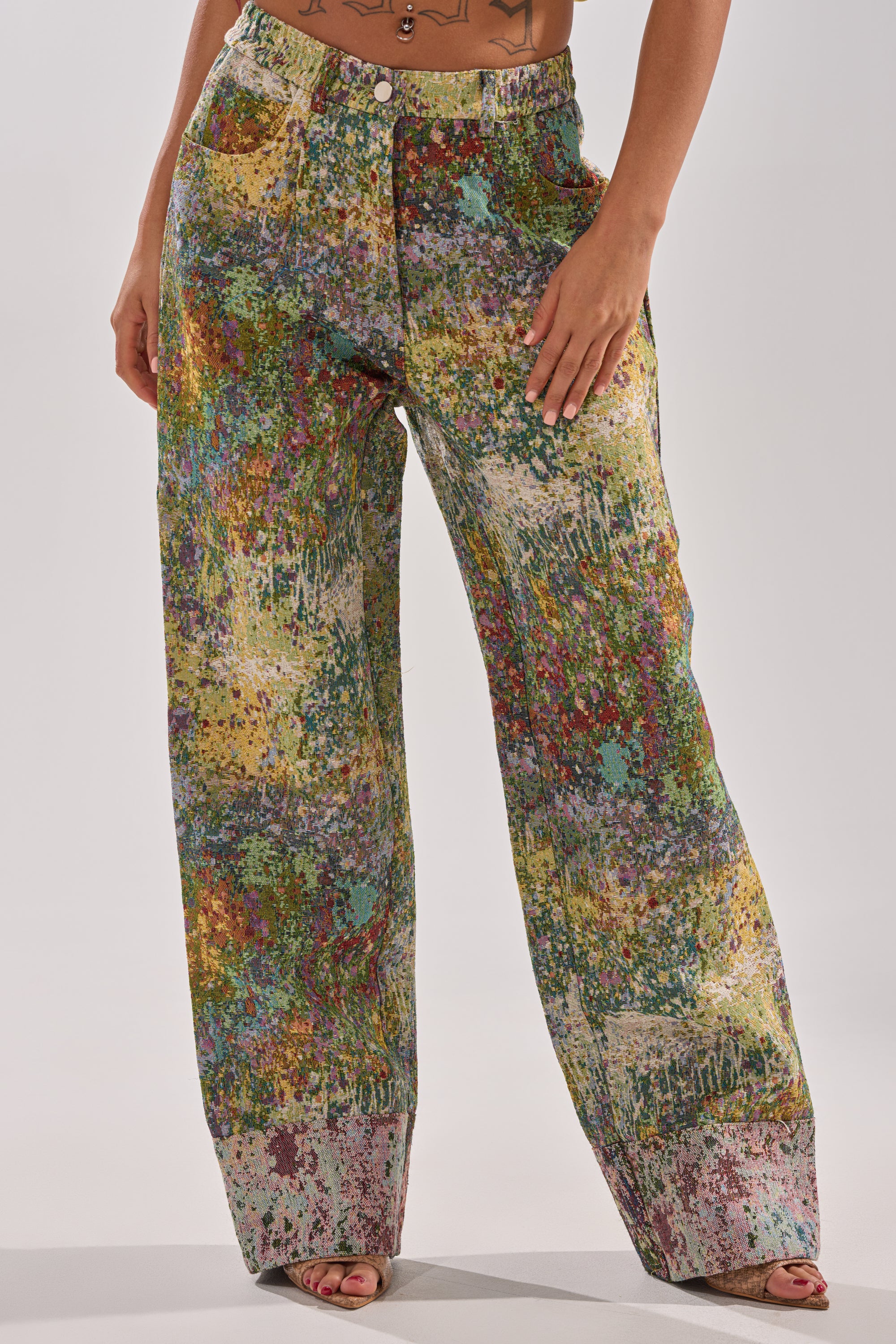 A person stands confidently with one hand on their thigh, wearing the DEEP IN THE SEA BROCADE TROUSER, featuring a high-rise, wide-leg silhouette and a vibrant, abstract paint-splatter print.