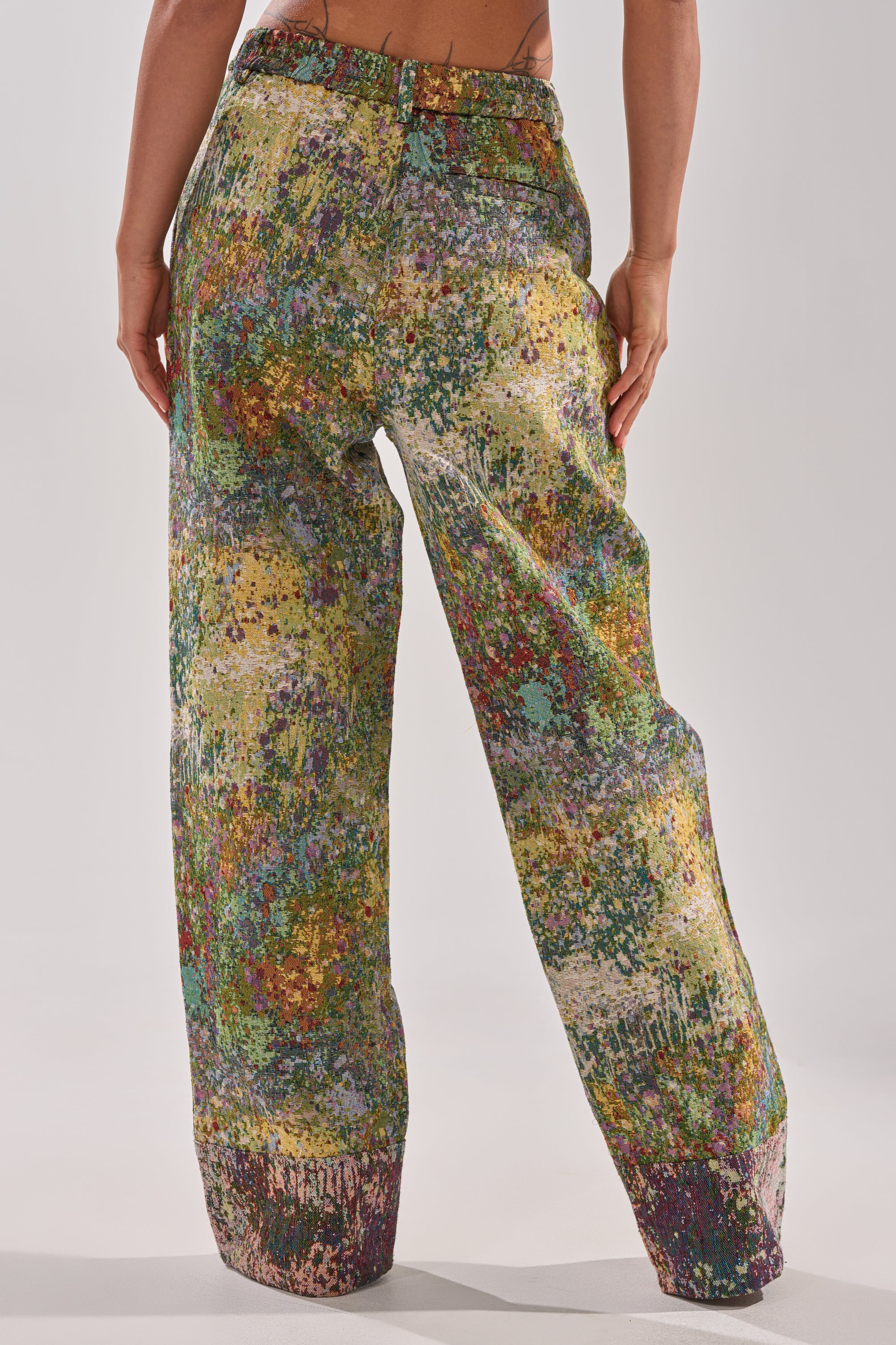 A person models the DEEP IN THE SEA BROCADE TROUSER—loose-fitting, high-rise pants with a vibrant abstract paint-splatter design—standing with their back to the camera against a plain light background.