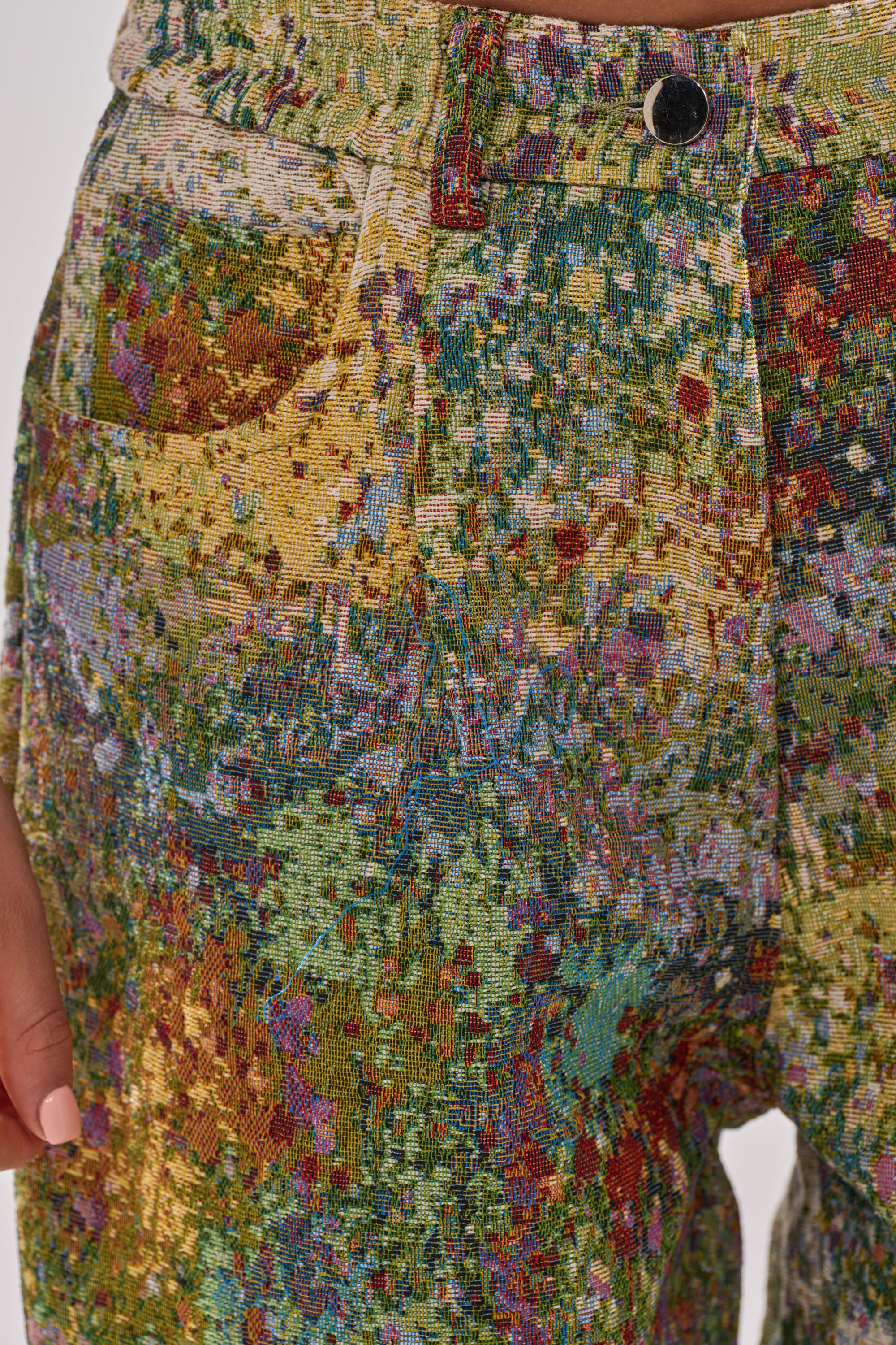 Close-up of the DEEP IN THE SEA BROCADE TROUSER featuring wide legs and a vibrant, abstract, paint-splatter-inspired pattern; a hand with light nail polish rests beside the pocket.