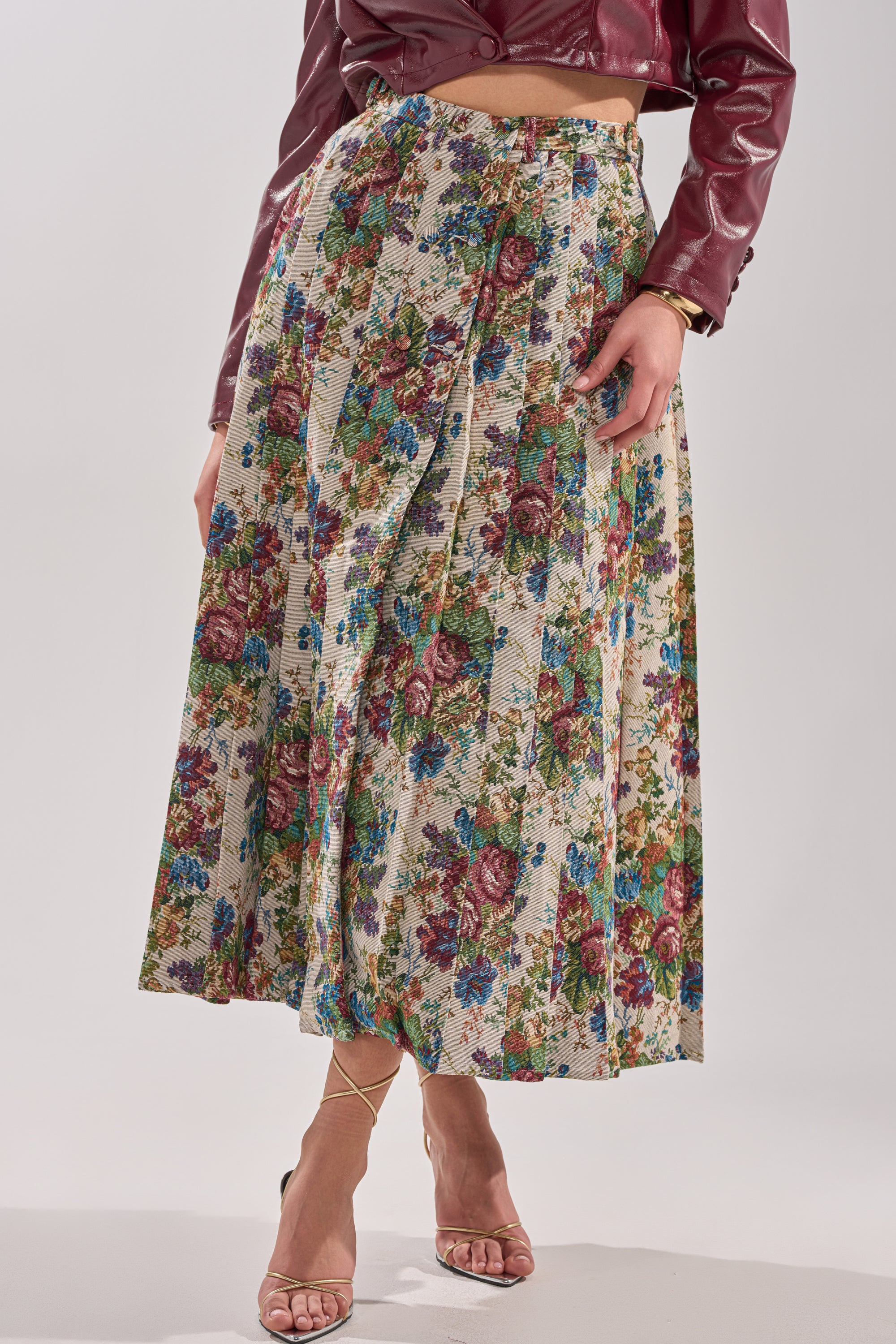 A person wears the TIFFANY BROCADE MAXI SKIRT, a high waist floral maxi with a multicolored pattern, paired with a maroon cropped jacket and strappy nude high-heeled sandals. 1