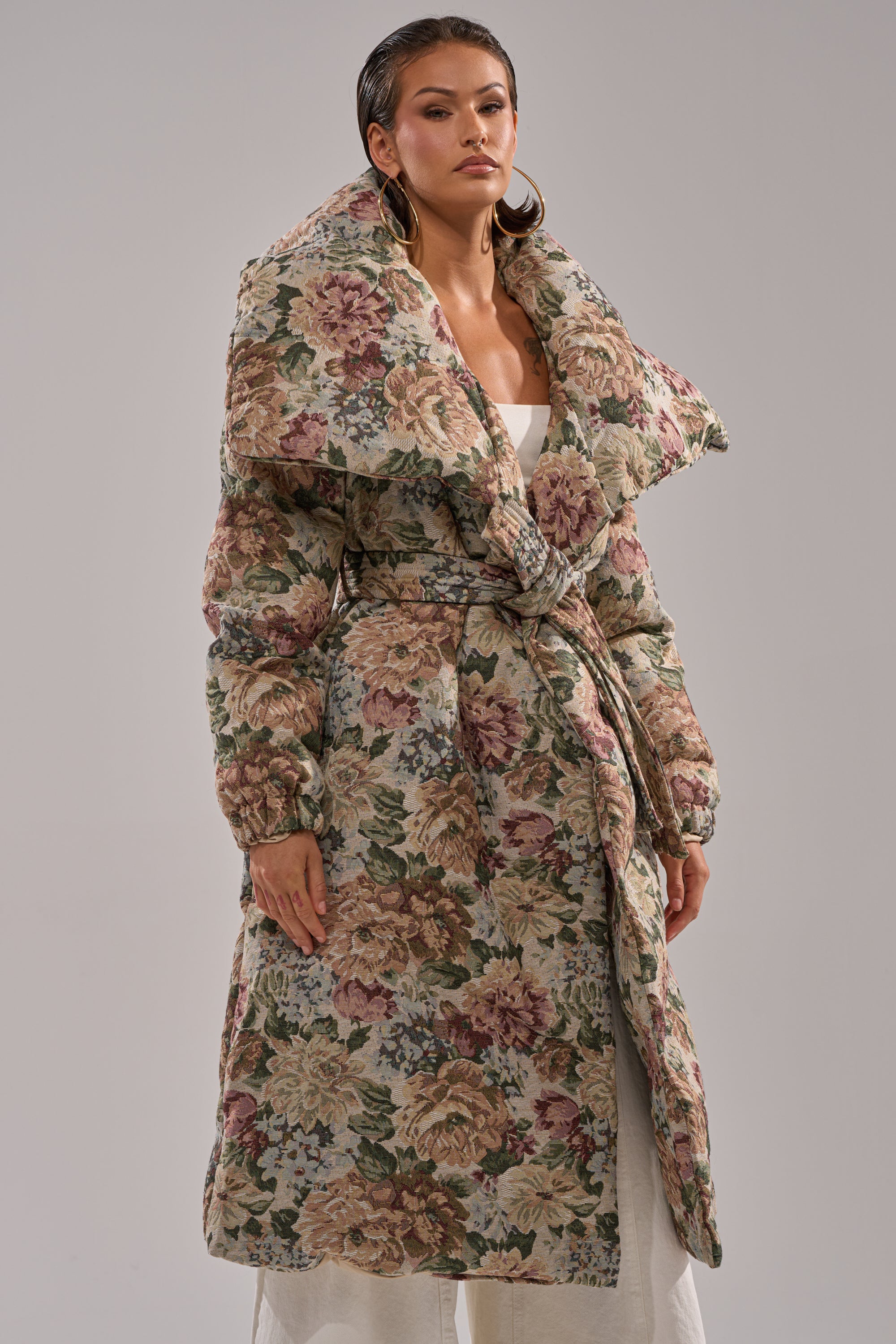 A person wears the I'M OUTSIDE TAPESTRY PUFFER, featuring a bold tapestry design and large collar, standing confidently against a plain background.