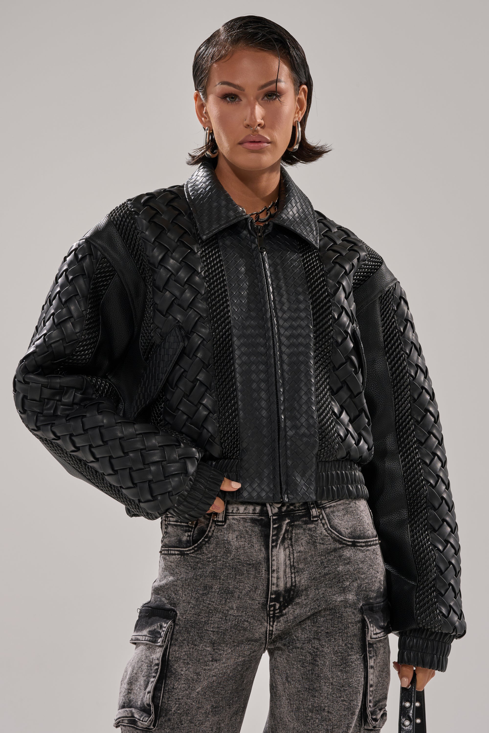 A person with short dark hair wears the KEEP IT LOWKEY PATCHWORK BOMBER and light gray cargo pants, standing against a plain light gray background with a confident expression.