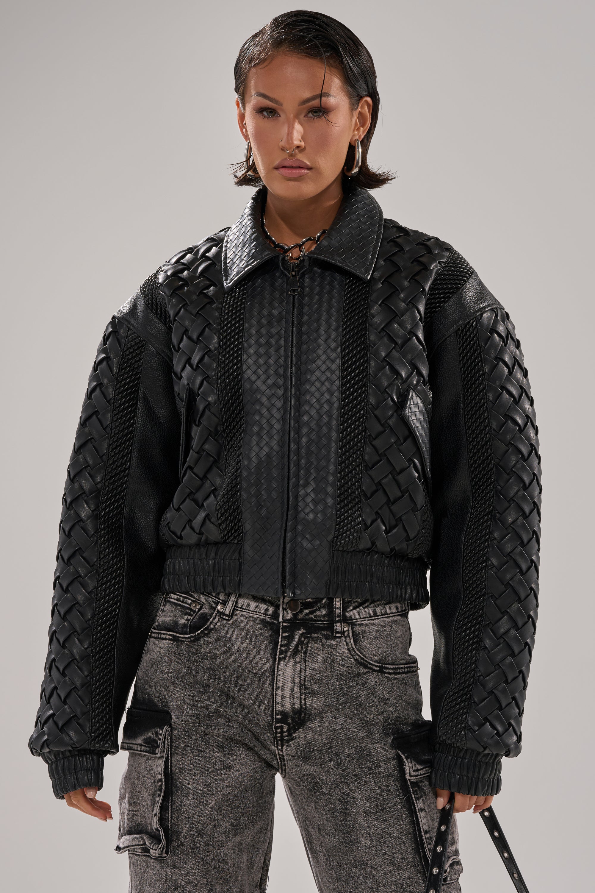 A woman with short dark hair wears the KEEP IT LOWKEY PATCHWORK BOMBER and gray acid-washed cargo jeans, standing facing forward with a neutral expression against a plain background.