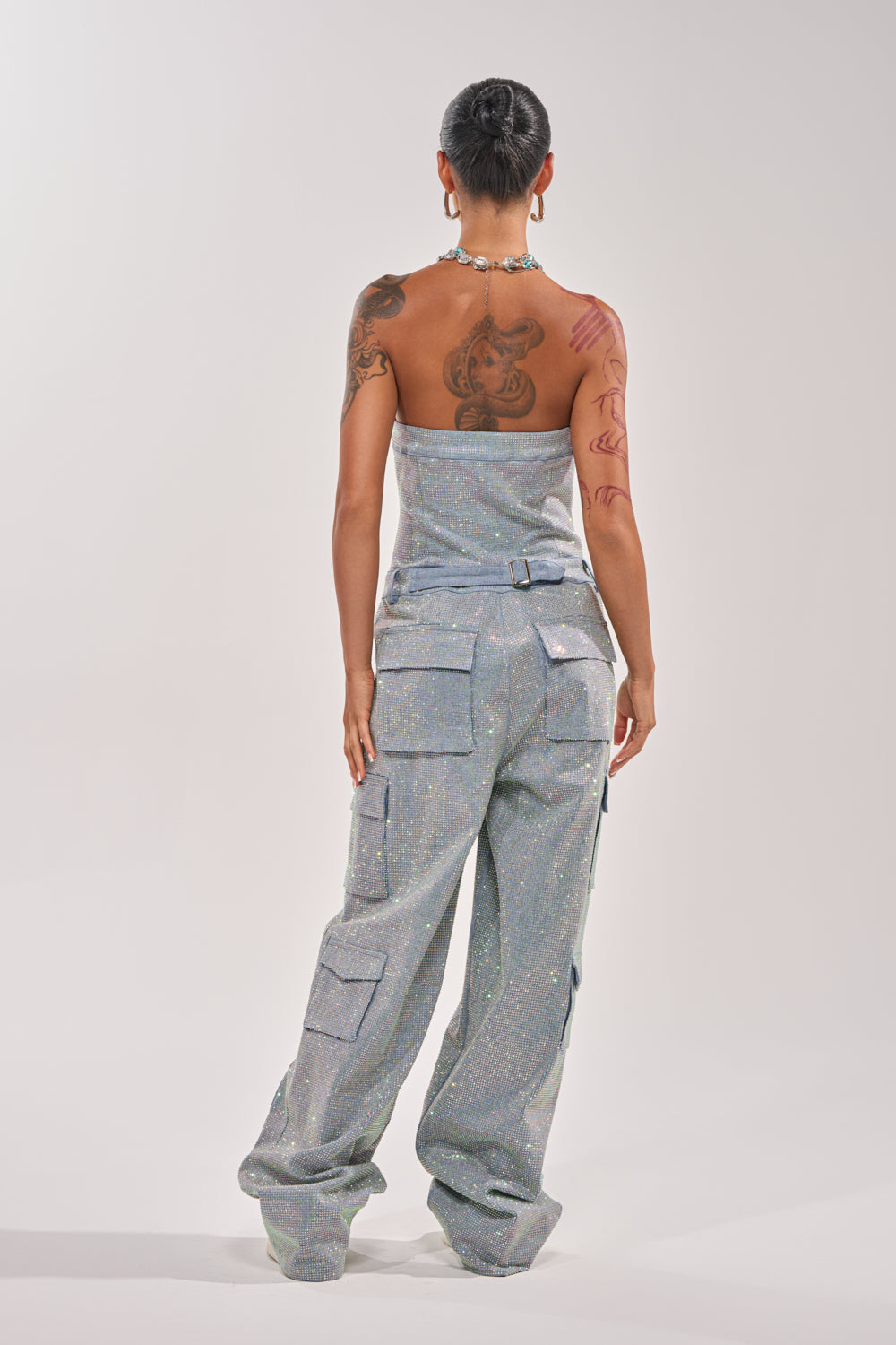 A person with tattoos and short dark hair models the TOO FLY RHINESTONE DENIM JUMPSUIT, featuring a strapless design and cargo pockets, standing with their back to the camera against a plain light background. 7