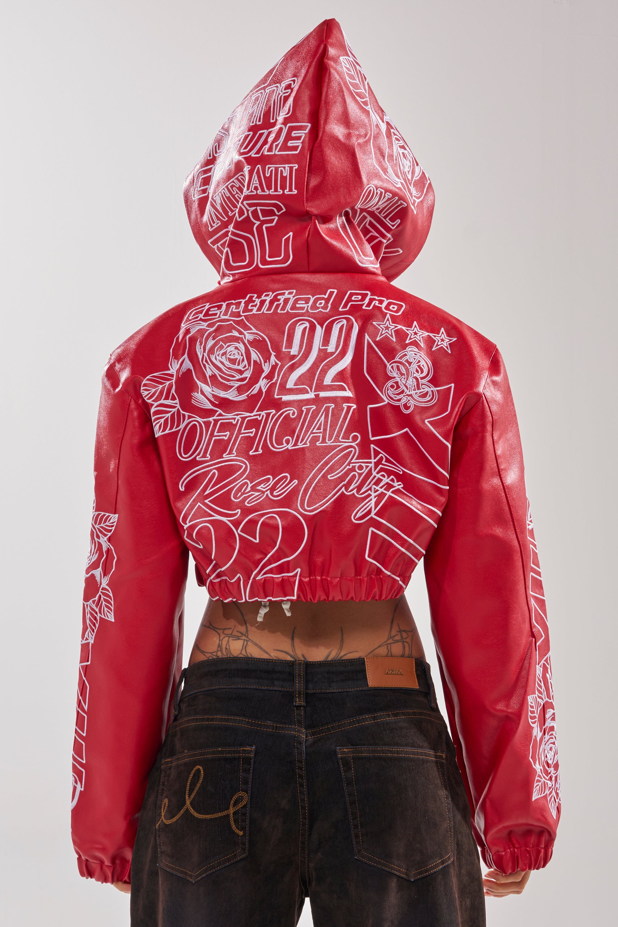 Wearing the PAINT THE TOWN RED EMBROIDERED BOMBER, a red cropped jacket with bold white “Certified Pro,” “22,” and “Rose City” text on the back, styled with high-waisted dark jeans for an edgy streetwear look. 6