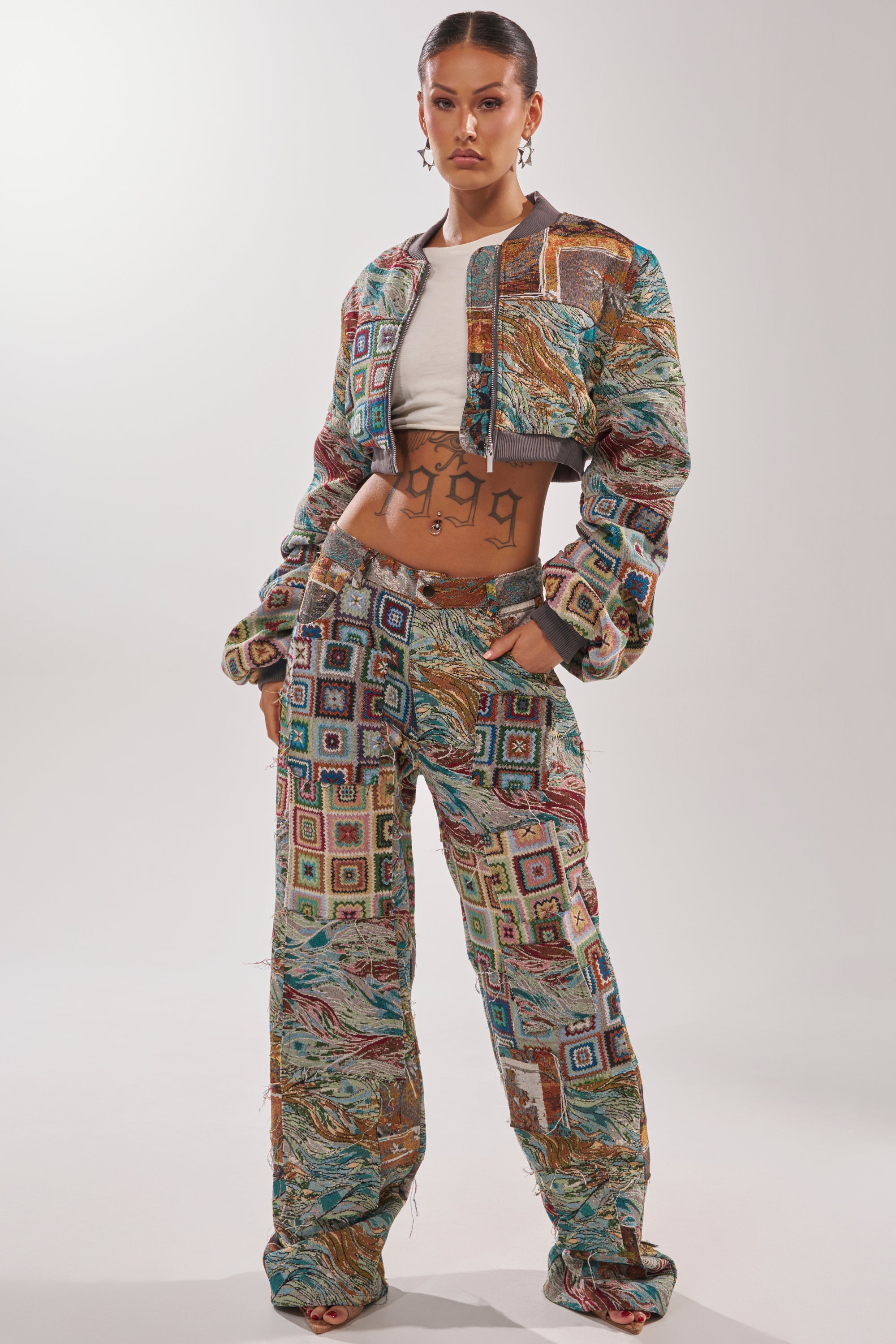 A woman poses in the WILD CROPPED PATCHWORK BOMBER and matching wide-leg pants over a white crop top, revealing her tattooed midriff against a plain, light background. 5