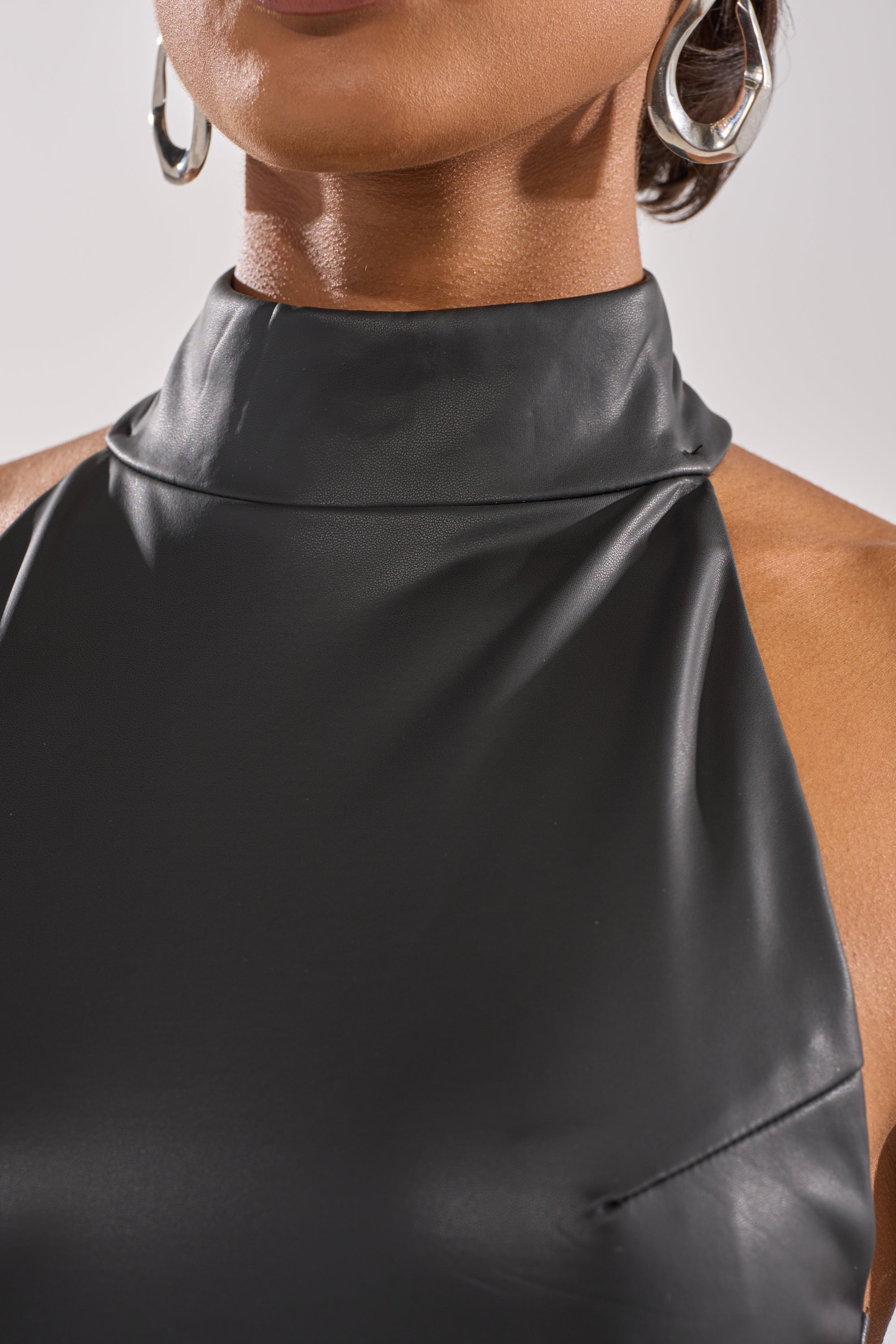 A close-up of a person wearing the sleeveless, high-neck RISKY BUSINESS LEATHER MAXI DRESS with large silver hoops, focusing on the neckline and upper chest to highlight its sleek, body-contouring design.
