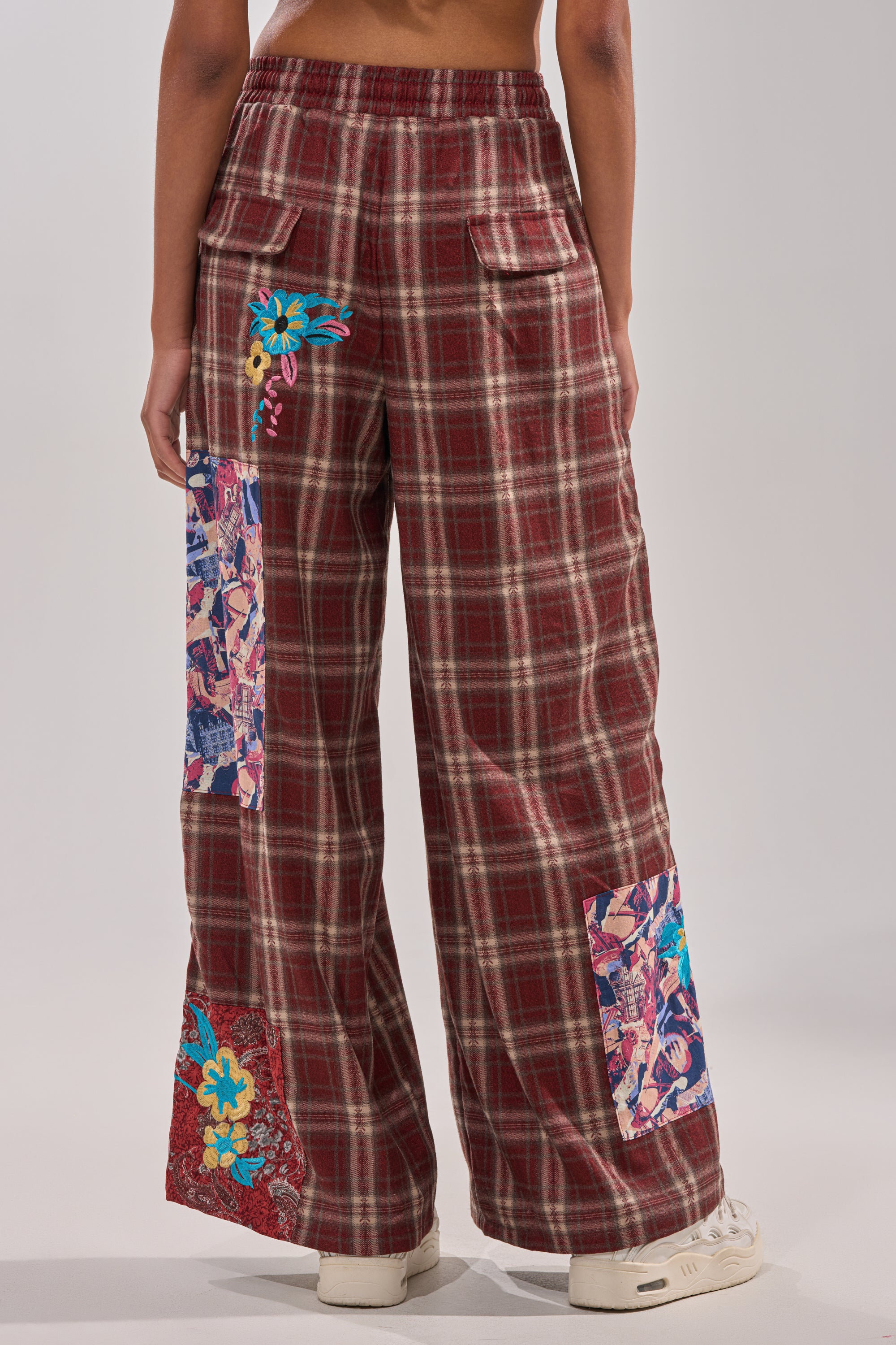 A person wearing the KRIYSTA FLORAL PATCH PLAID PANT stands facing away, showcasing the back details and their white sneakers. 5