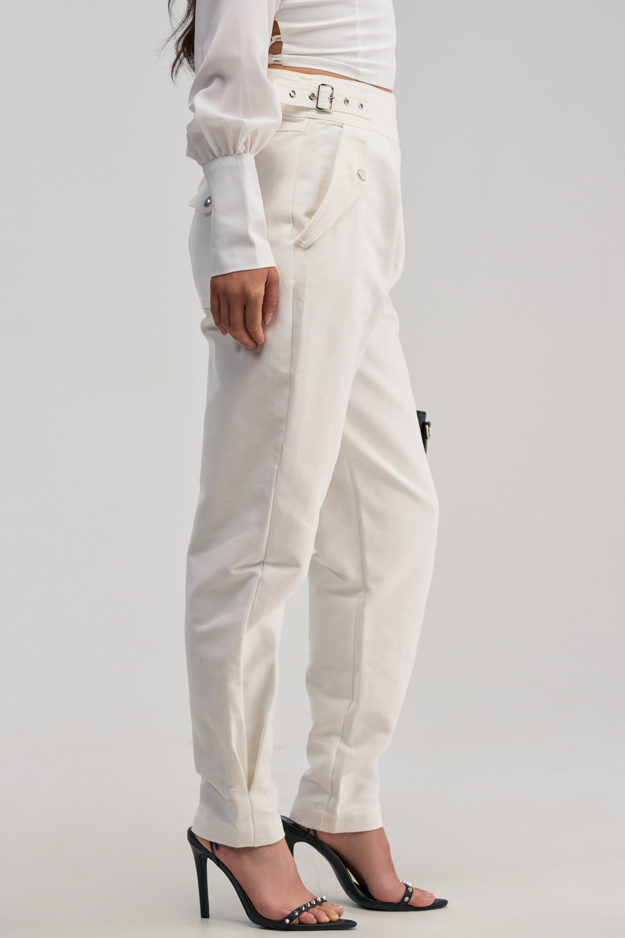 A person wearing a white long-sleeve shirt, the HEY YOU TROUSER with a belt, and black high-heeled sandals, standing against a plain light background.