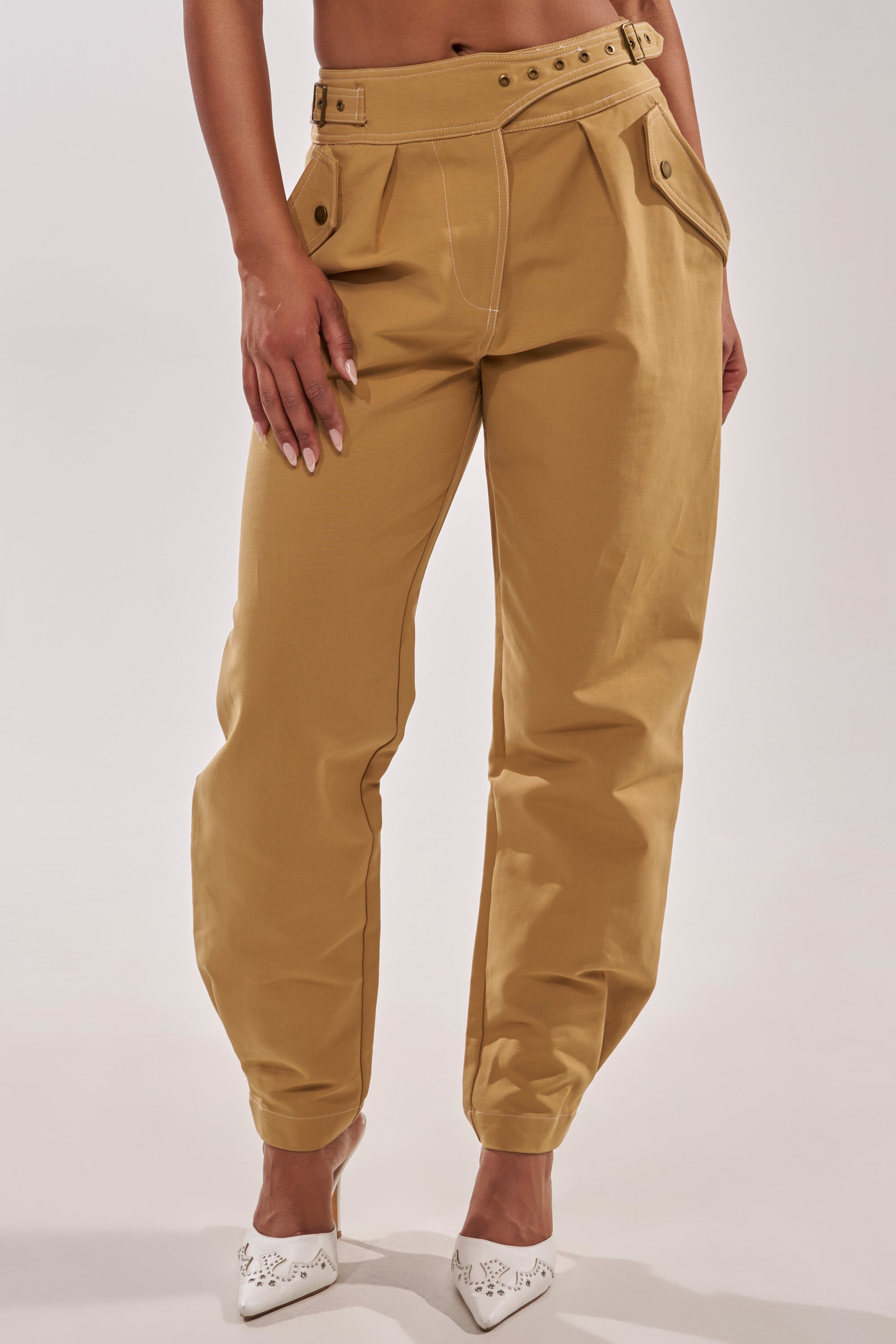 A person wearing HEY YOU TROUSER, a pair of high-rise cotton trousers with a matching belt, and white pointed-toe flats stands against a plain light background. 0