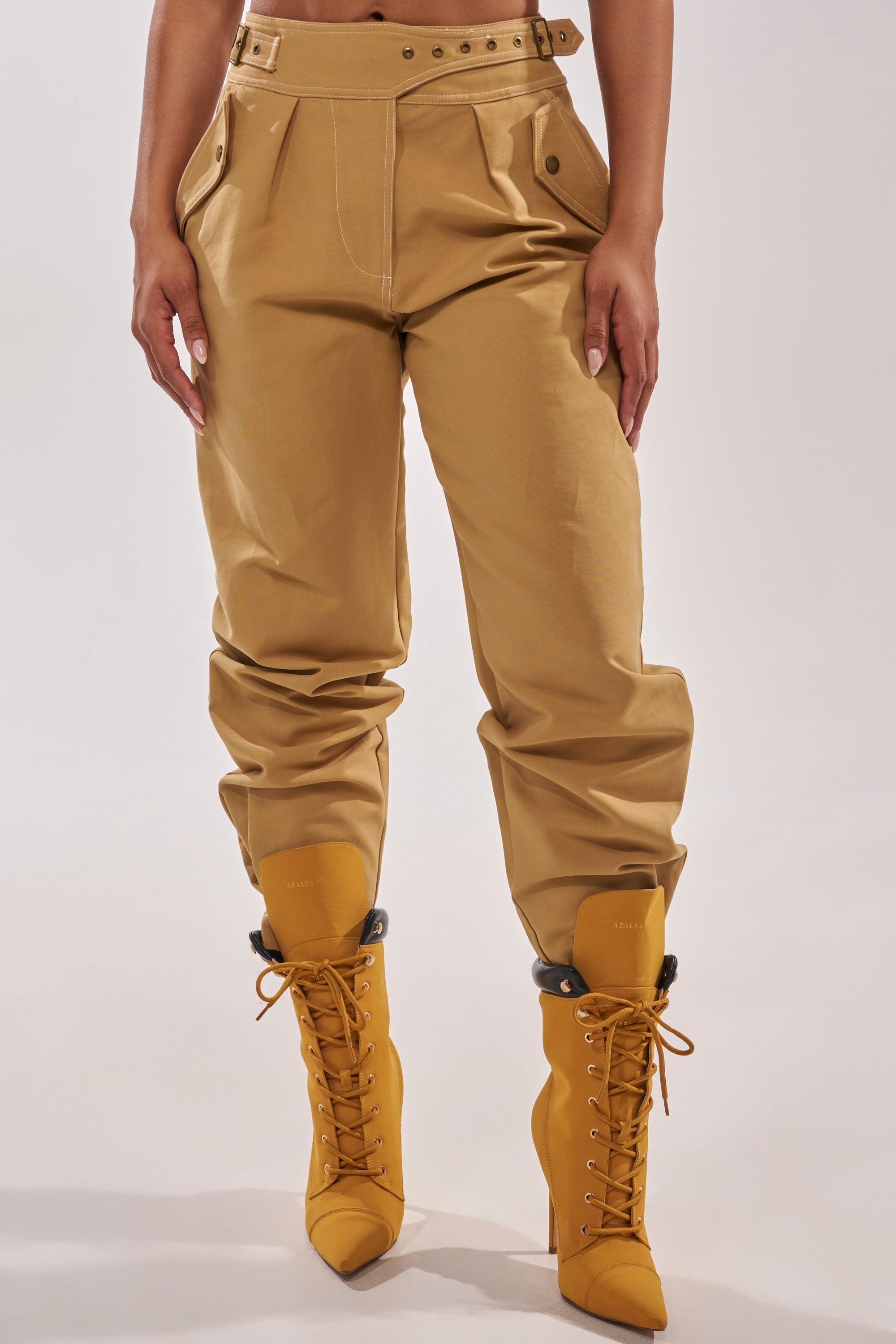 Model wears the HEY YOU TROUSER—high-rise tan pants with white stitching—paired with matching tan lace-up heeled boots; only the lower torso and legs are visible against a plain background. 1