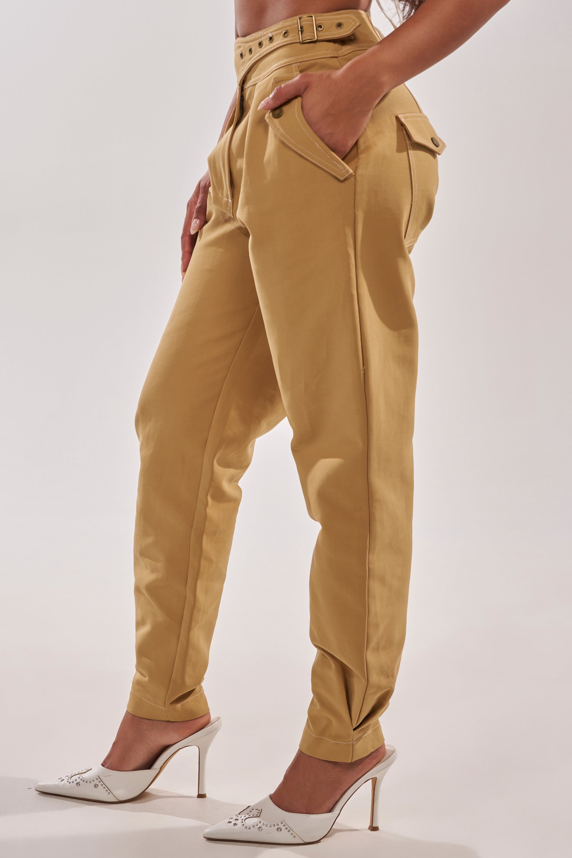 A person stands with one leg slightly forward against a plain light background, wearing HEY YOU TROUSER with a matching belt and white heeled mules. 3