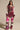 A woman faces forward in ONLY THE COOLEST RHINESTONE PANT, featuring a high-rise fit, chevron and leopard print accents, shiny pink, white and burgundy hues, flared legs, and a glittery finish. Long-sleeved top has striped cuffs.