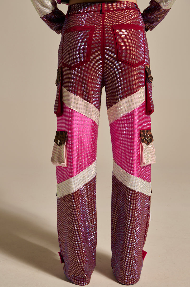 Person seen from behind wearing ONLY THE COOLEST RHINESTONE PANT: shiny, high-rise sequin cargo pants in pink, purple, and white with maroon trim, large back pockets, and several side cargo pockets—full length visible.