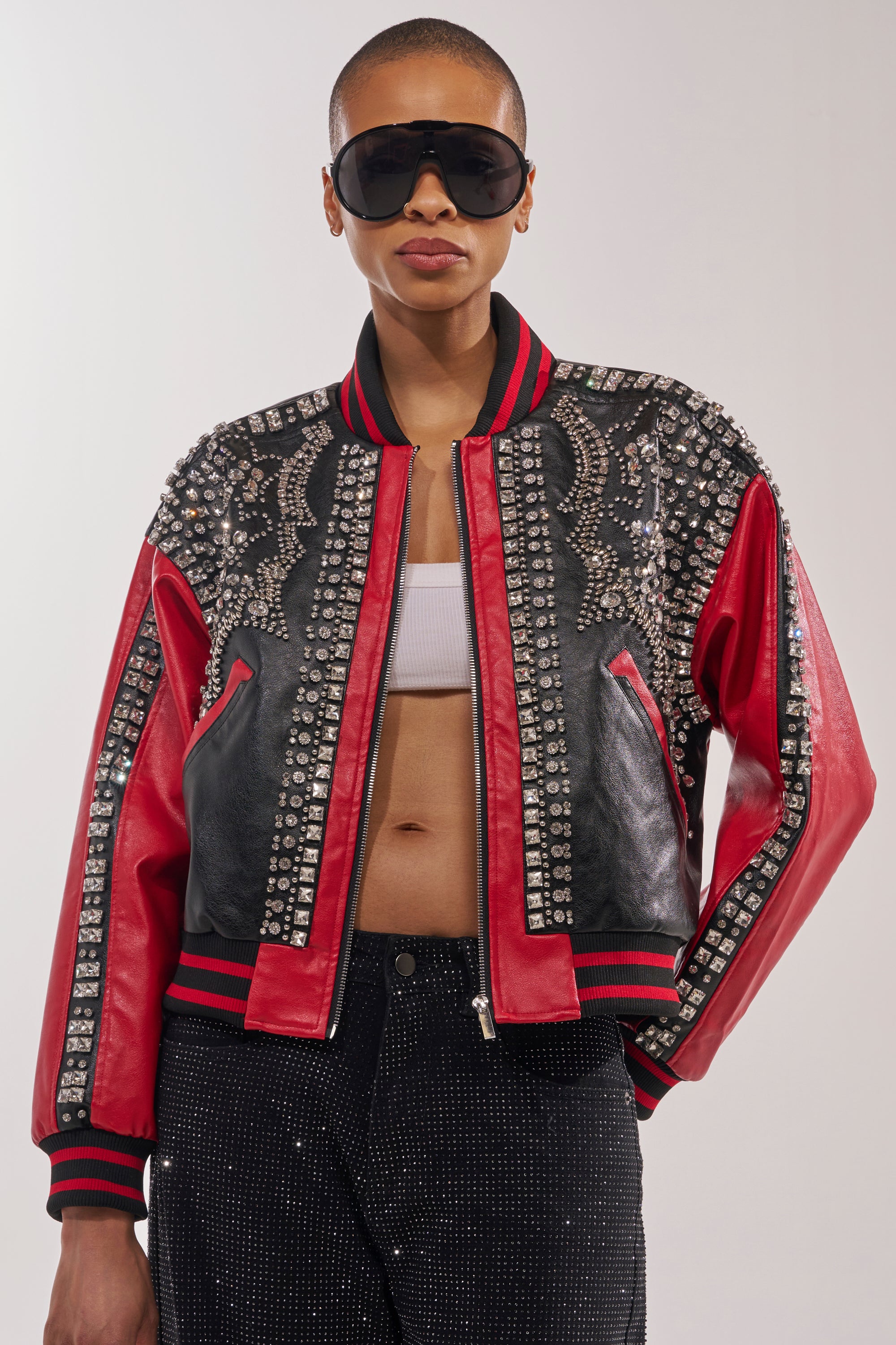 A person wearing oversized sunglasses, black sparkly pants, a white crop top, and the STOLE THE SHOW EMBELLISHED BOMBER stands confidently against a plain background. 1