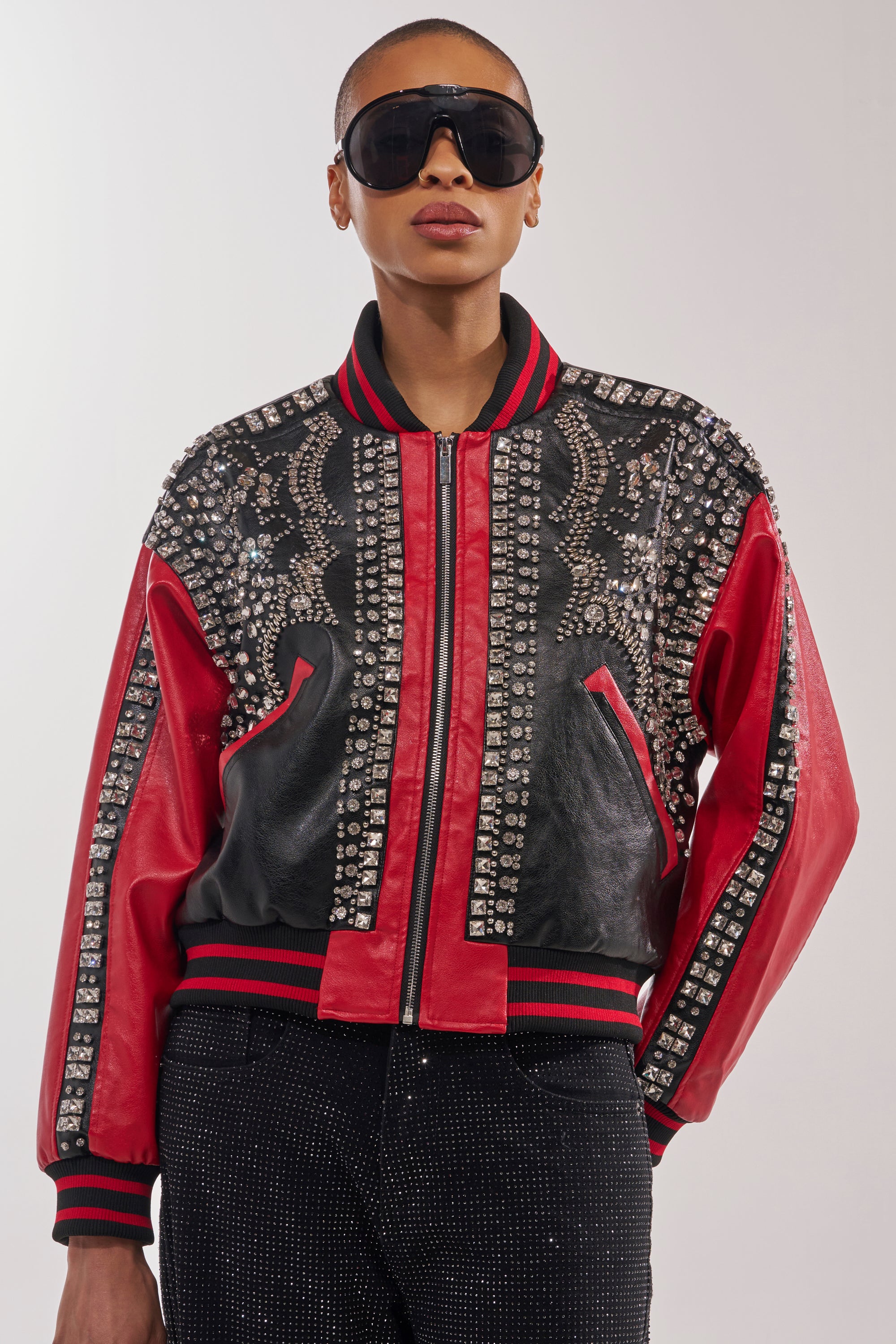 A person stands against a plain light background wearing black pants, large black sunglasses, and the STOLE THE SHOW EMBELLISHED BOMBER with intricate silver details in black and red. 2