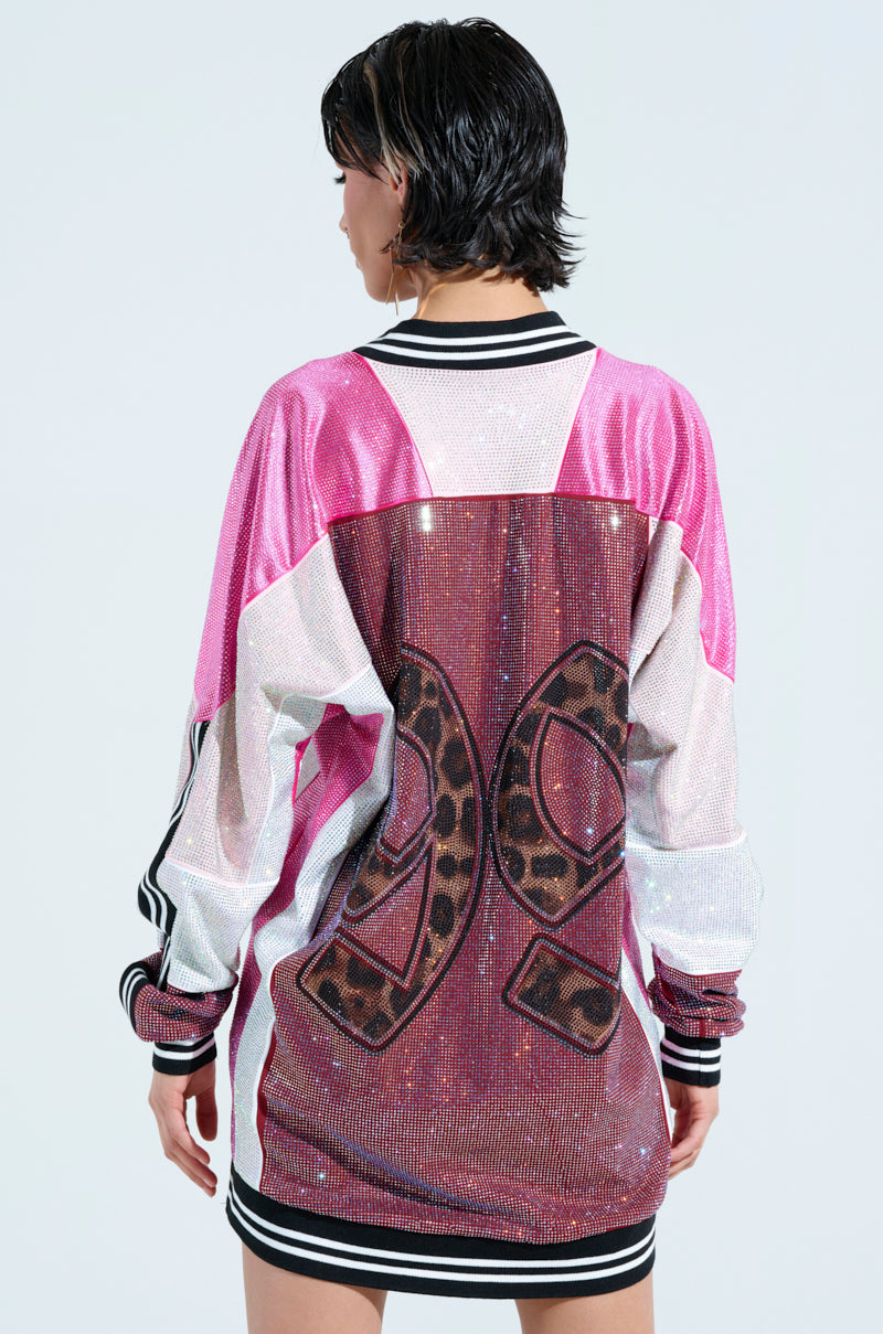 A person with short hair is wearing an ONLY THE COOLEST RHINESTONE JERSEY DRESS in shiny pink and white, featuring striped cuffs and a large leopard print number "29" on the back, set against a plain light-colored background.