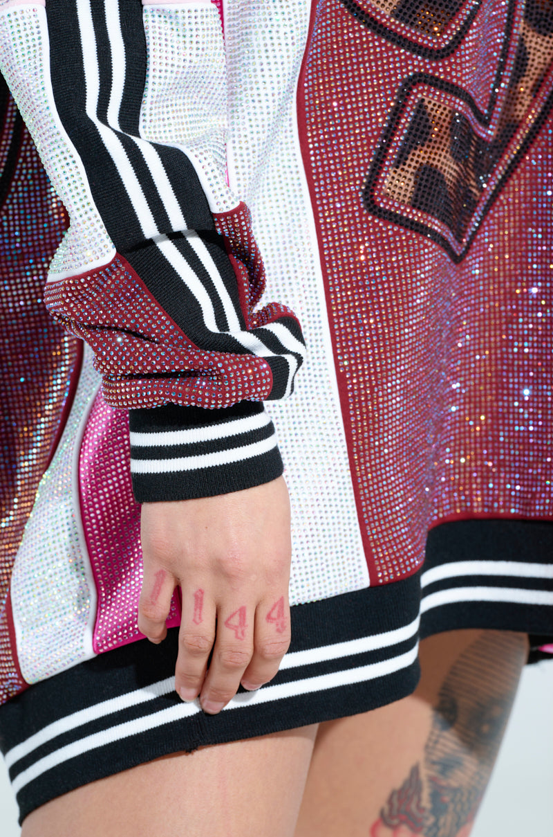 Close-up of a hand with "4AD" written on the fingers, touching an ONLY THE COOLEST RHINESTONE JERSEY DRESS in sparkly pink and black, featuring stripes and a leopard print number. Tattoos are partially visible on the thigh at the bottom.