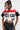 A woman gazes sideways, wearing the OFFICIAL DUTY CROPPED BUTTON DOWN TOP featuring bold text and a touch of color block pattern, paired with black shorts. Her long, straight hair is styled in a half-up-do, complementing the stylish and casual ensemble against a plain background.