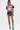 A person exudes confidence in an OFFICIAL DUTY CROPPED BUTTON DOWN TOP, black shorts with chain details, and lace-up knee-high boots. The faux leather details add edge against a plain white background.