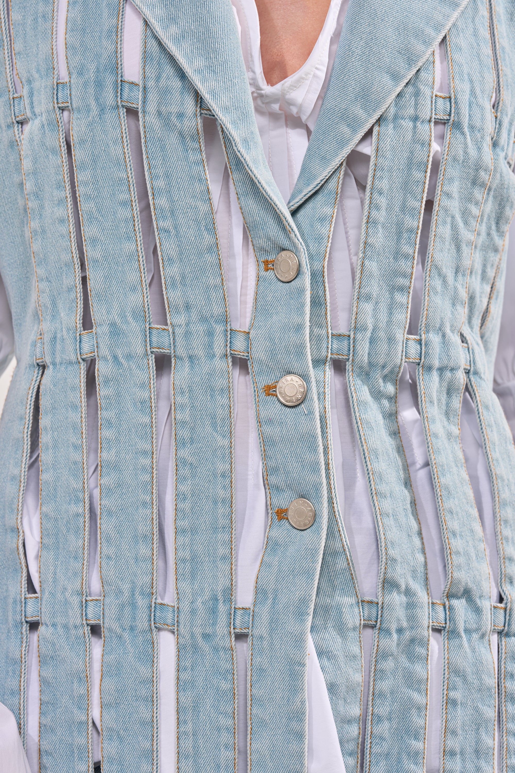 A close-up of the RIGHT THROUGH ME CUTOUT DENIM VEST, featuring silver buttons and vertical cutouts revealing a white layer underneath, styled street-chic over a white shirt. 10