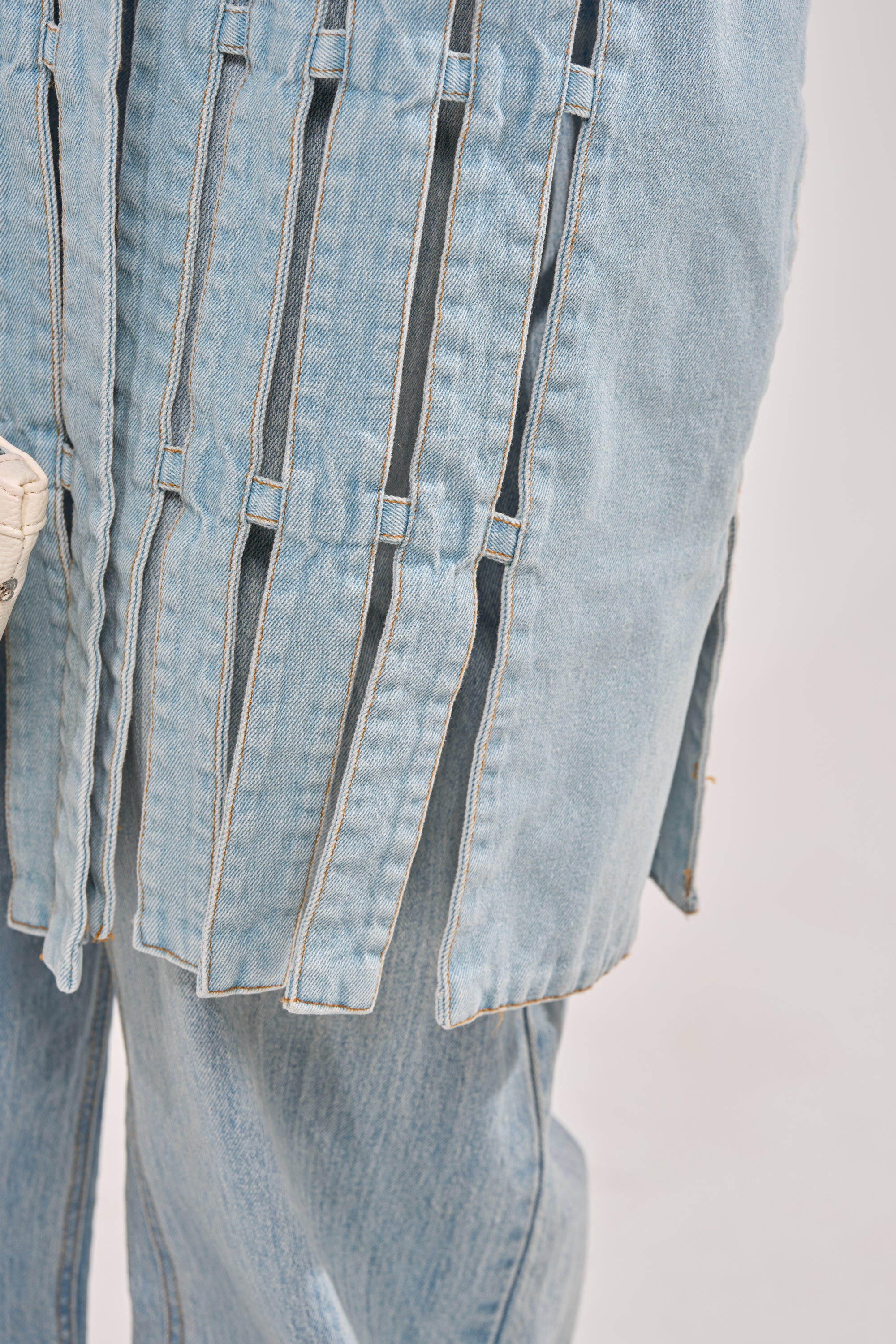 Close-up of the RIGHT THROUGH ME CUTOUT DENIM VEST in light blue, featuring vertical slits and loose-hanging strips. Another denim layer shows beneath, adding a modern, distressed street-chic vibe. 11