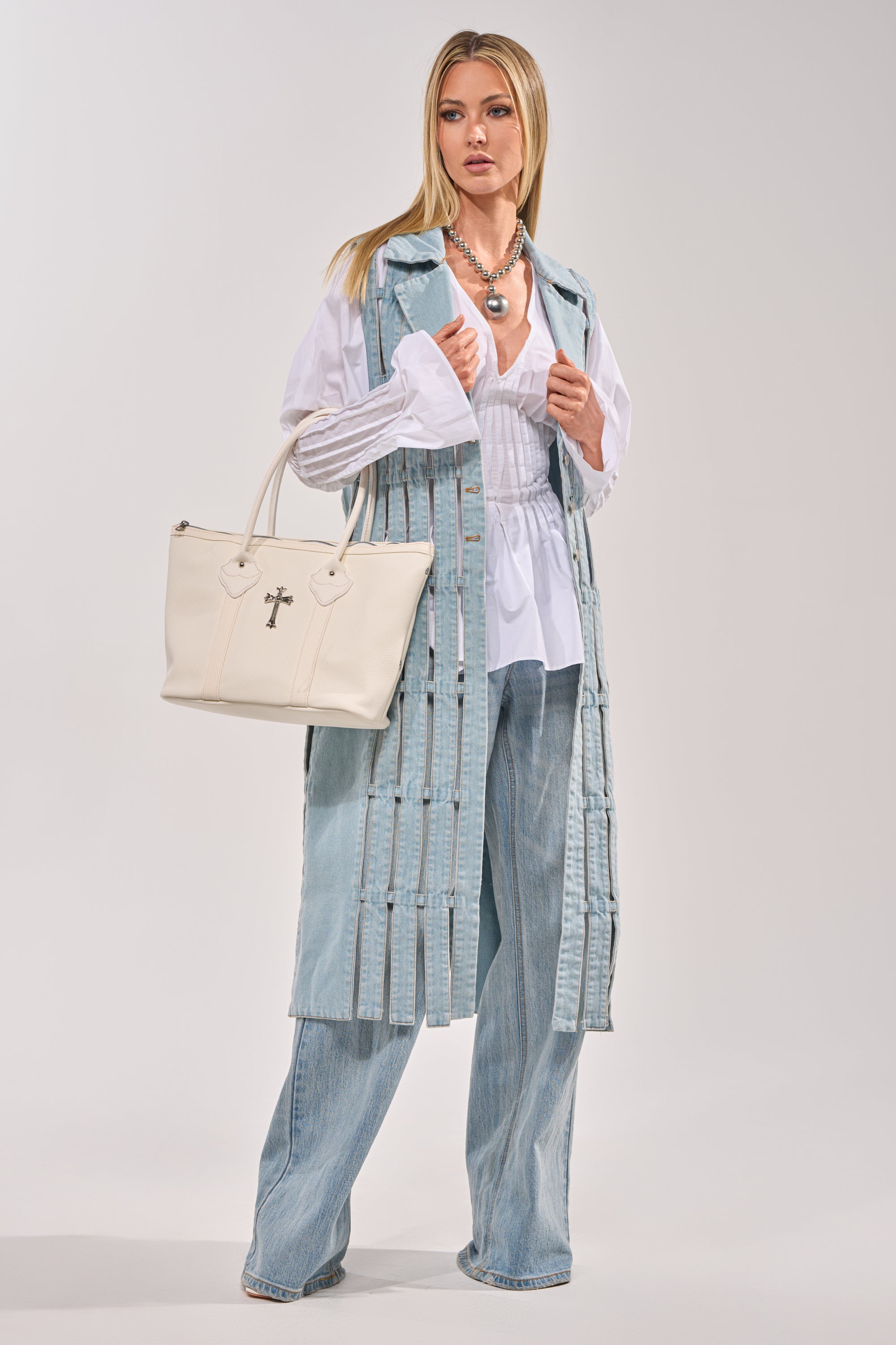 A woman wears the RIGHT THROUGH ME CUTOUT DENIM VEST over a white blouse and wide-leg jeans, accessorized with layered necklaces and a white crossbody handbag. The backdrop is plain and light-colored. 8