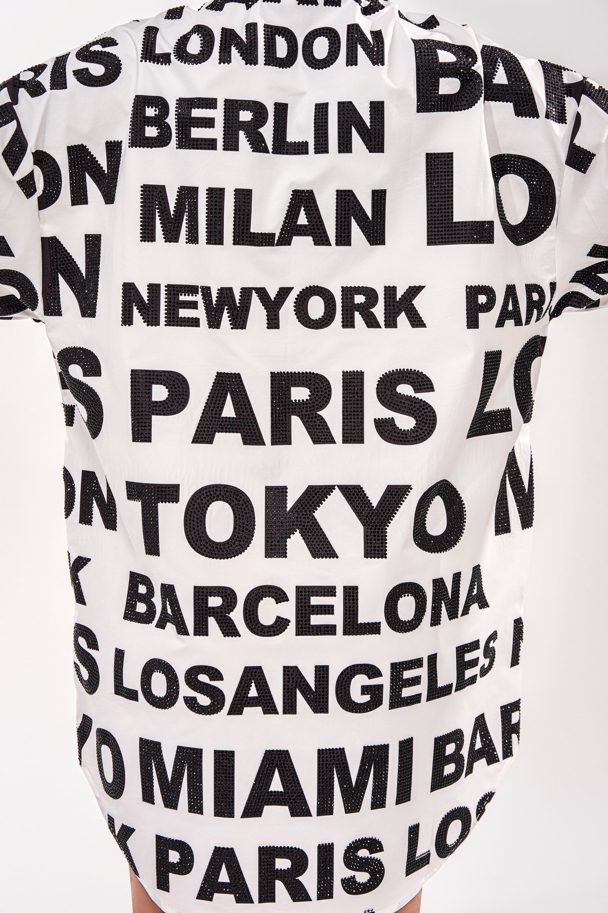 The TIME AND PLACE POPLIN MINI DRESS is a white mini shirt dress with bold black text featuring major cities like London, Berlin, and Paris for a striking black-and-white graphic statement look. 11