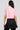 A person with long brown hair is wearing the FEMME RACING BUTTON DOWN POPLIN SHIRT IN PINK and a short black skirt. They are facing away from the camera against a plain background.