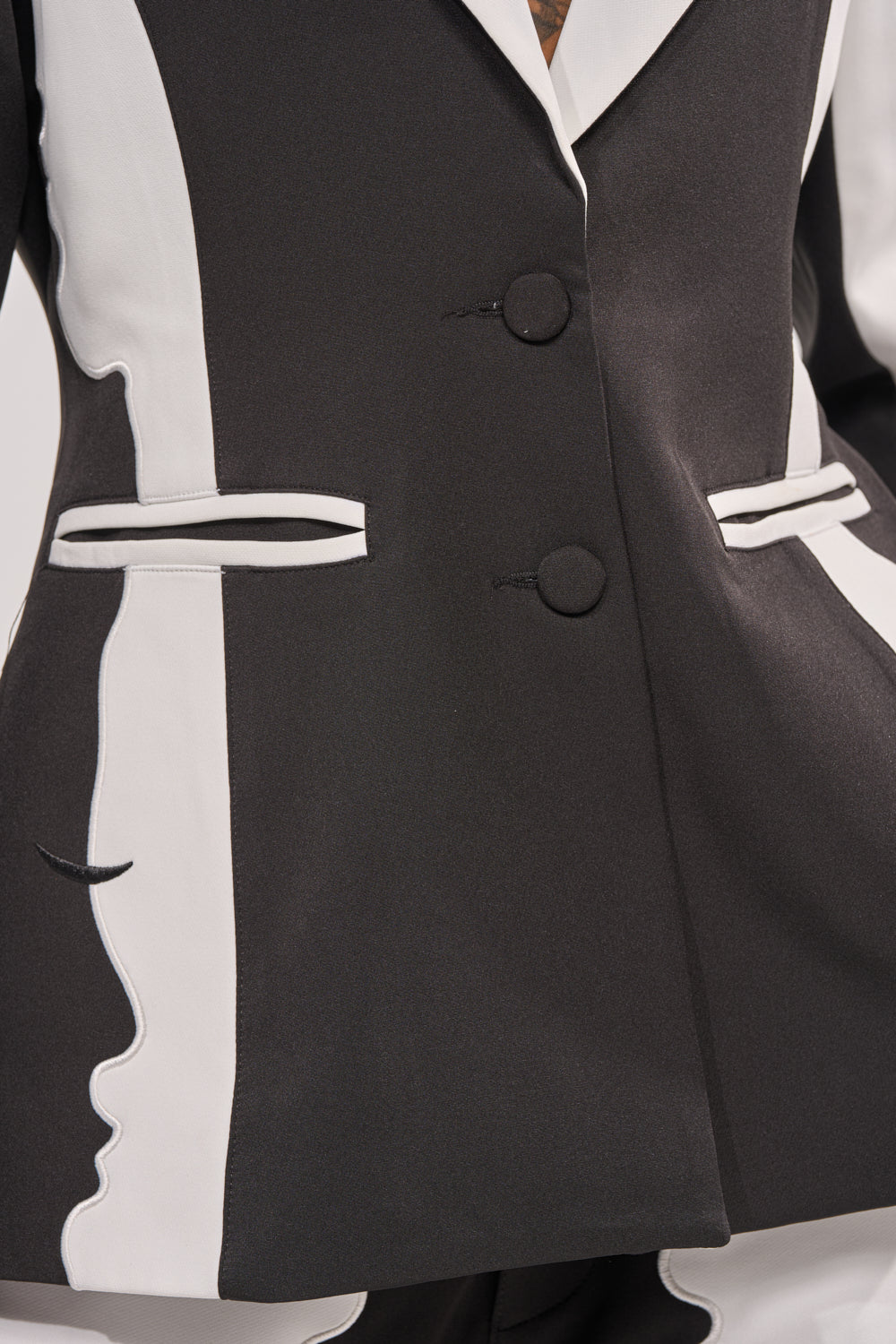 Close-up of the POV GRAPHIC BLAZER in black and white, showcasing abstract color-block side panels with a profile face design, two buttons, and two horizontal front pockets. 11
