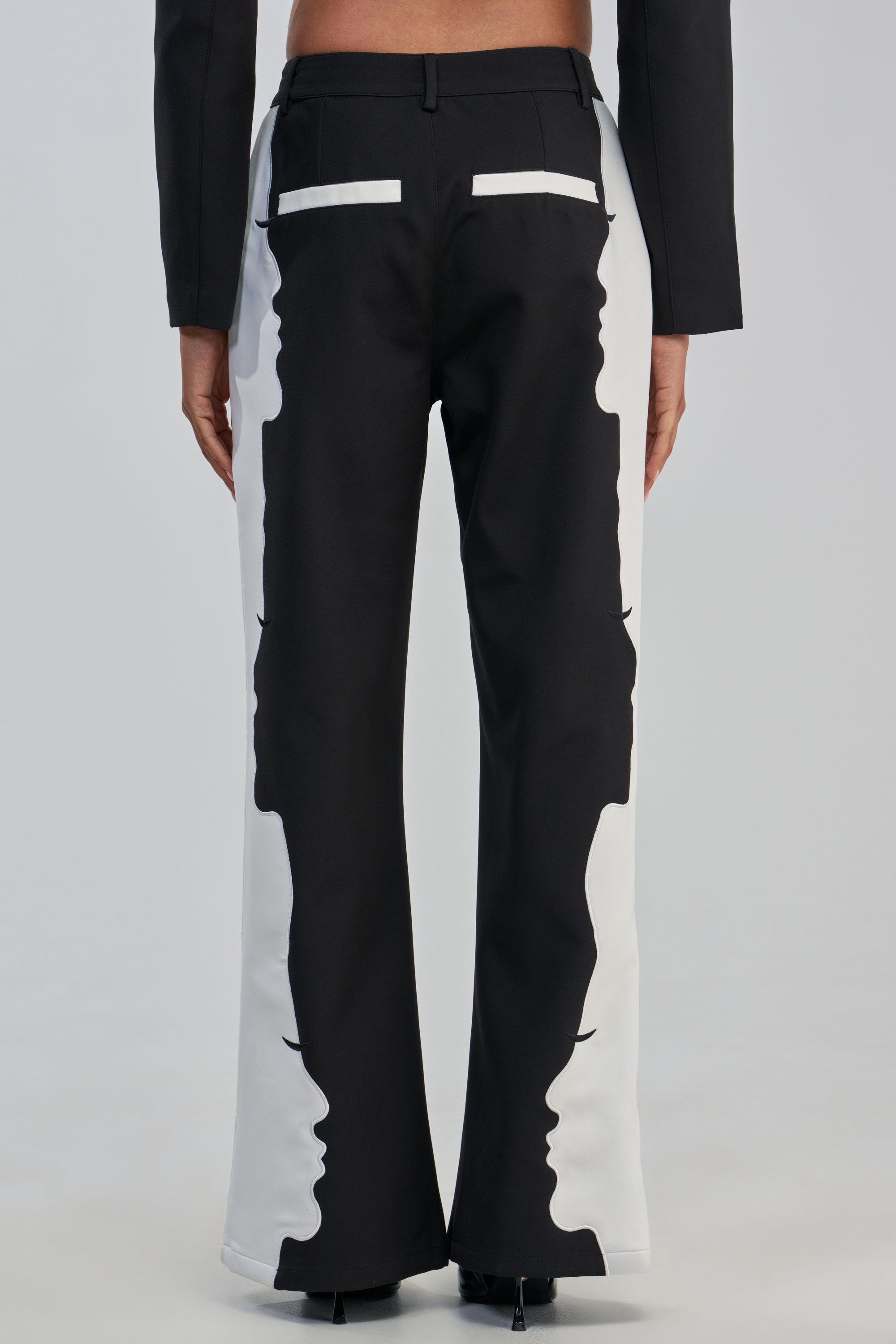 A person viewed from the back is wearing the POV GRAPHIC TROUSER—high-rise wide-leg pants in black and white, featuring a distinctive side profile face graphic running down each leg.