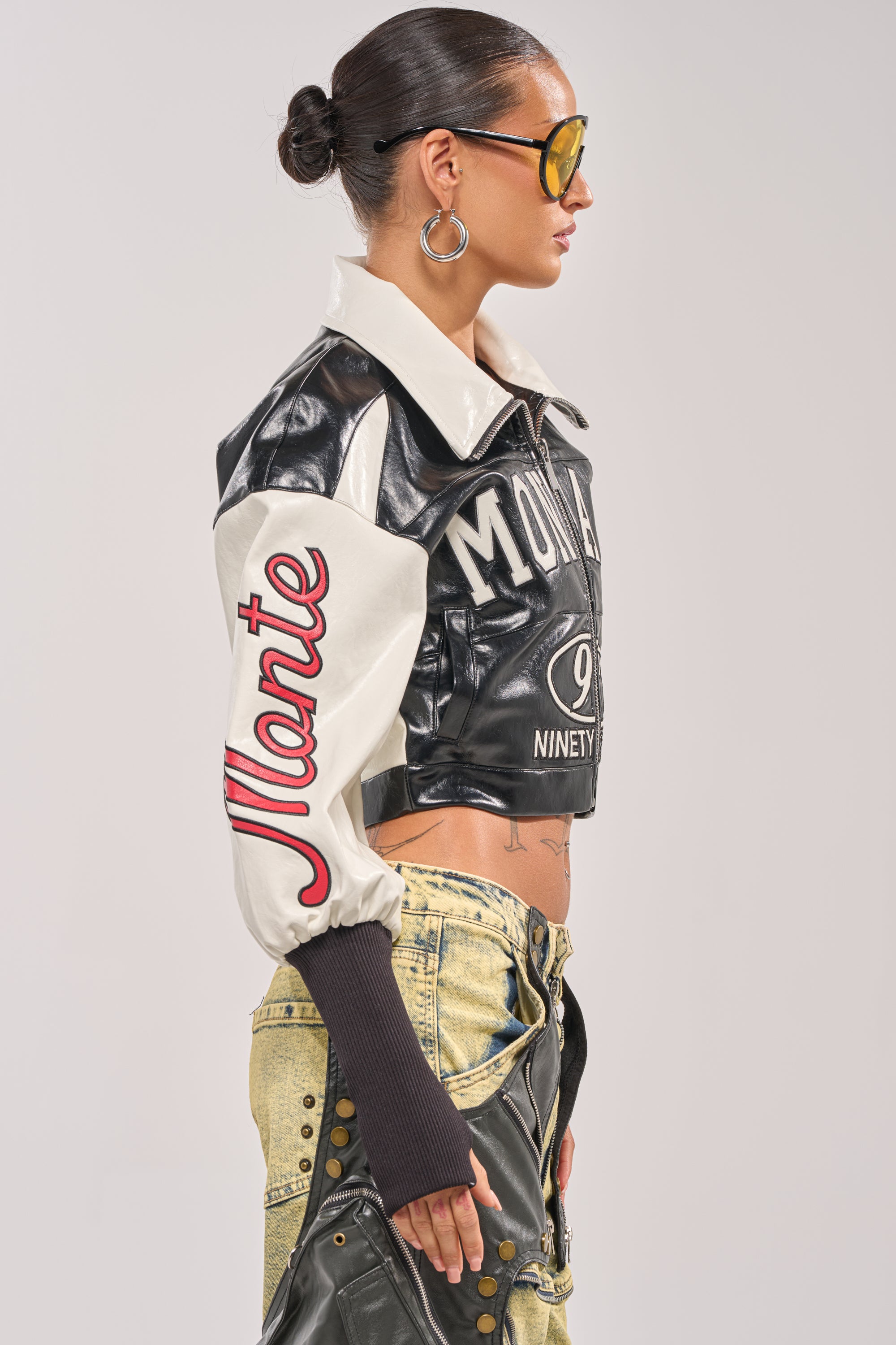 A woman in profile wears sunglasses, large hoop earrings, the LET'S RACE EMBROIDERED BOMBER with "Monte" on the sleeve, and beige distressed pants with black accents. 4