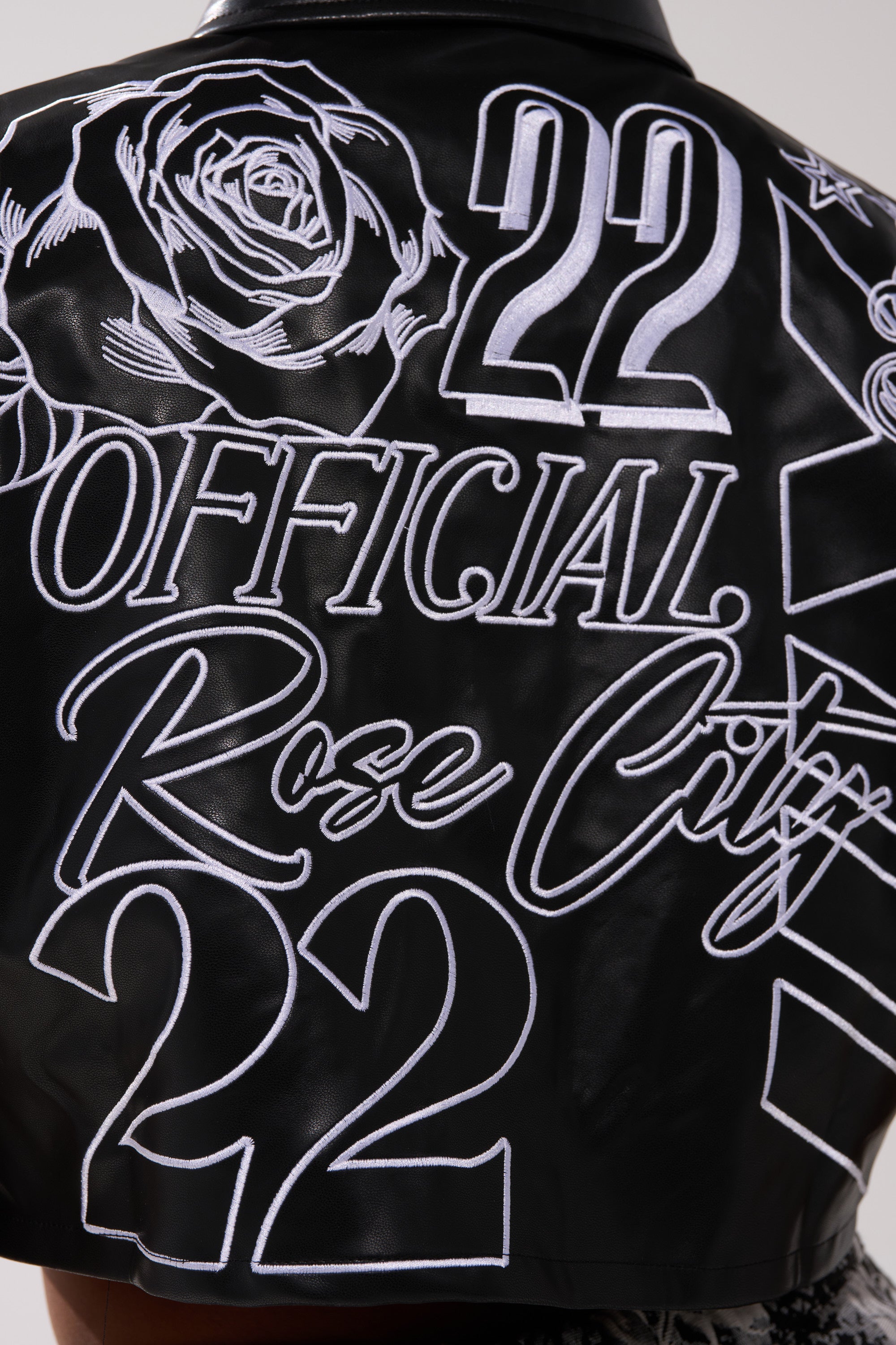 The MAKE IT OFFICIAL FAUX LEATHER BUTTON DOWN IN BLACK has white embroidery on the back, with a large rose, “OFFICIAL Rose City,” and the number “22” shown twice in both bold and cursive fonts.