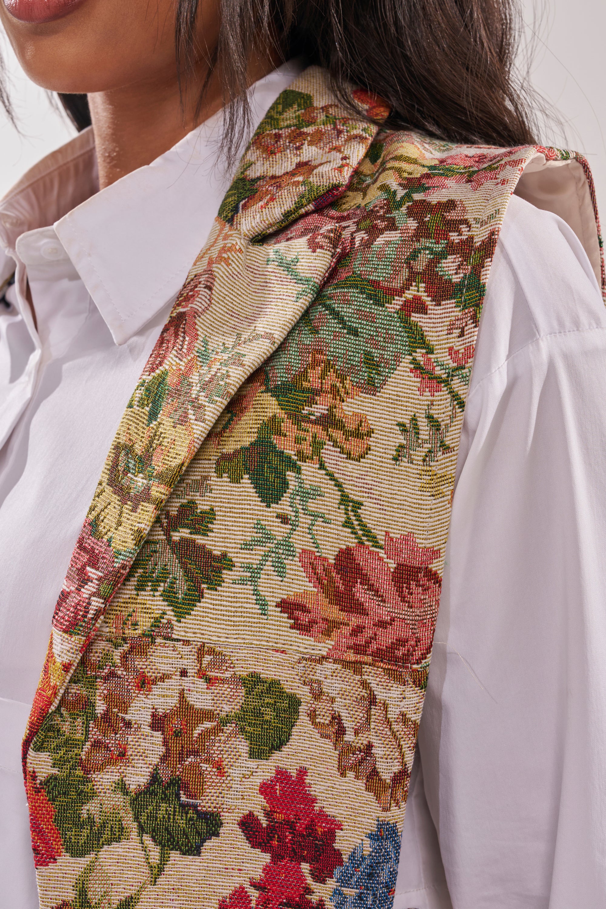A close-up of a person in a white collared shirt wearing the HONEY HONEY SPLIT VEST IN TAPESTRY, focusing on the vest’s intricate tapestry design and artistic flair, with the person's face partially visible. 6