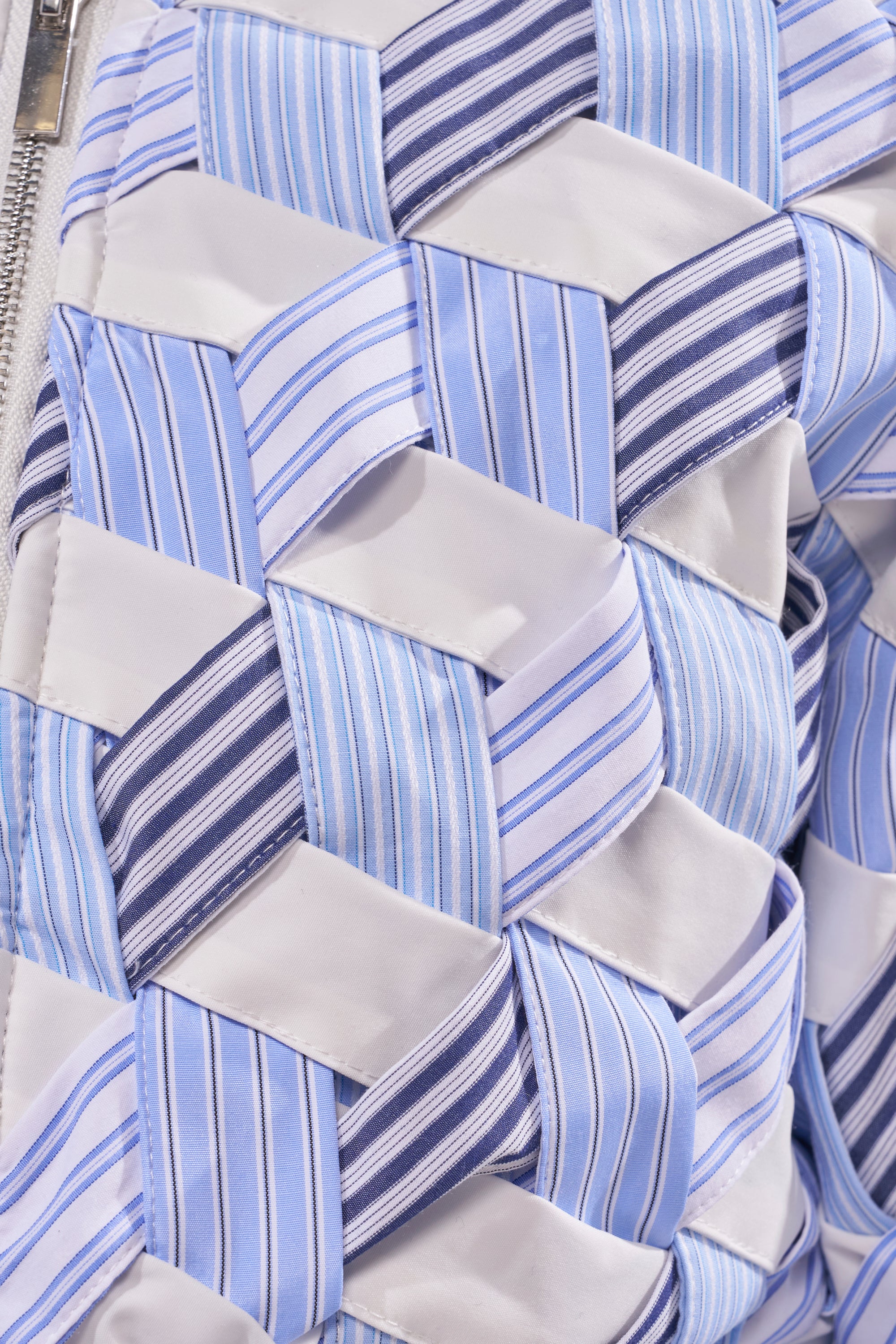 Close-up of the BOP AND WEAVE POPLIN BOMBER’s geometric woven pattern in blue, white, and stripes, featuring textured fabric strips and a visible left-side zipper. 6