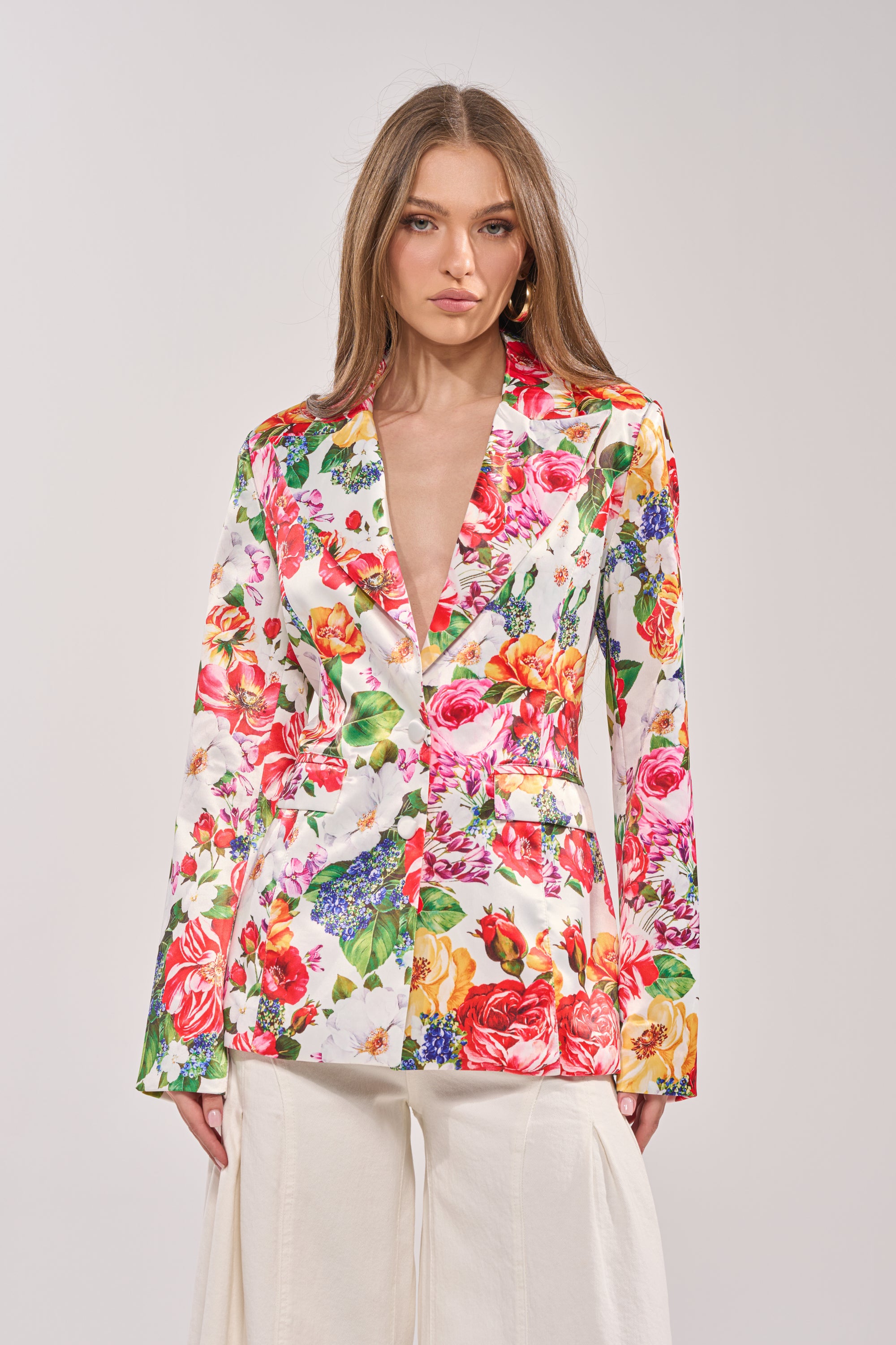 A woman with long, straight hair wears the ALESSANDRA SATIN BLAZER with wide lapels and white wide-leg pants, standing against a plain light background. 1