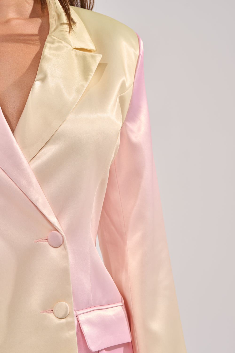 Close-up of a person wearing the SWEET TALK SATIN BLAZER, featuring a pastel cream and light pink gradient, notched collar, two buttons, and a flap front pocket for an elegant touch. 7