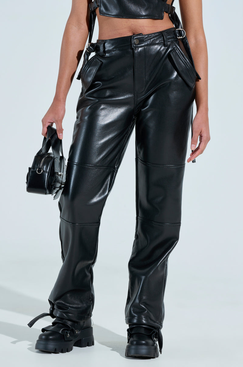 A person styled in high-rise black leather BEEN THE PRIZE FAUX LEATHER TROUSERs, paired with matching boots and holding a small black bag. The trousers are designed with a high waist and multiple zippers, set against a plain light background.