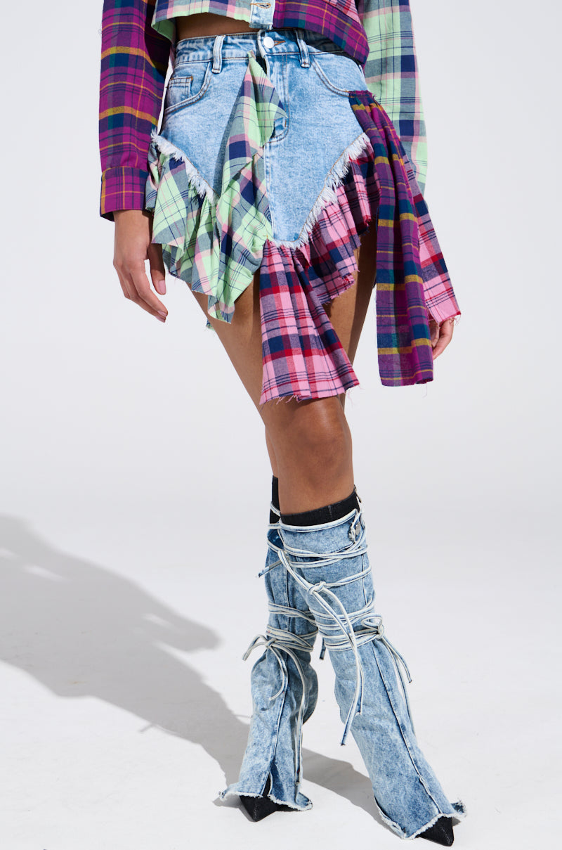 The ensemble features a colorful plaid shirt paired with frayed denim shorts and bell-bottom-style denim boots. White laces accentuate the boots, and the look is set against a plain white background. Note that the shorts are reminiscent of the THINK ABOUT ME MORE MINI SKIRT WITH PLAID DETAILS.