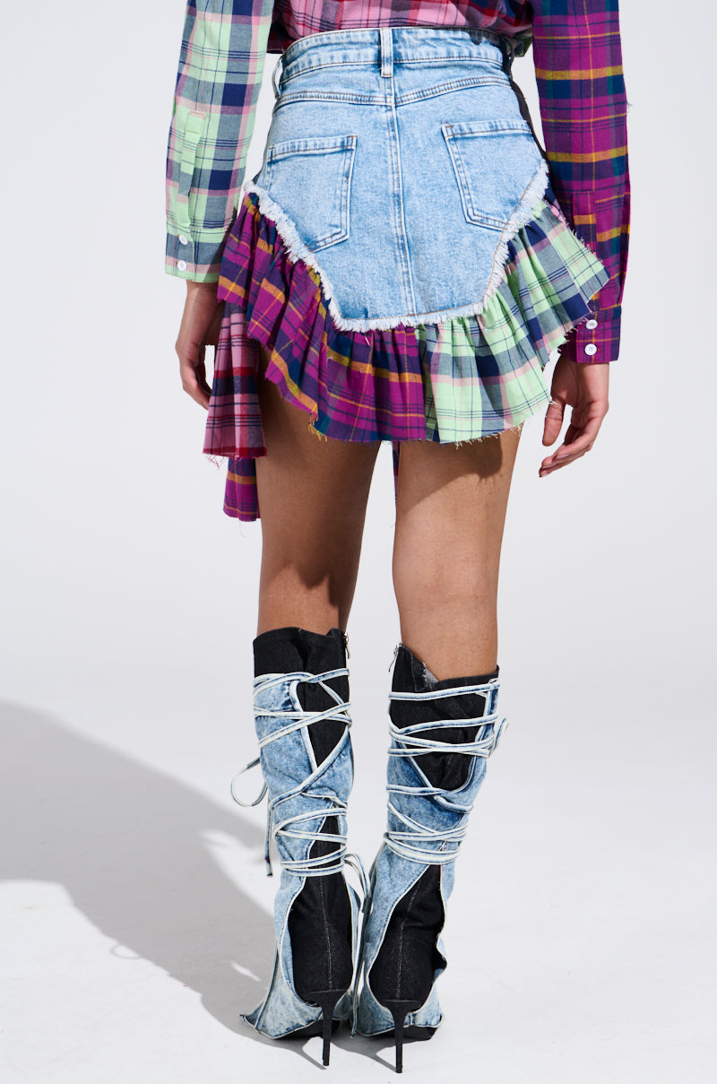 A person in the THINK ABOUT ME MORE MINI SKIRT WITH PLAID DETAILS, featuring frayed edges, wears a plaid shirt and high denim boots with black accents and white laces, standing against a plain background.
