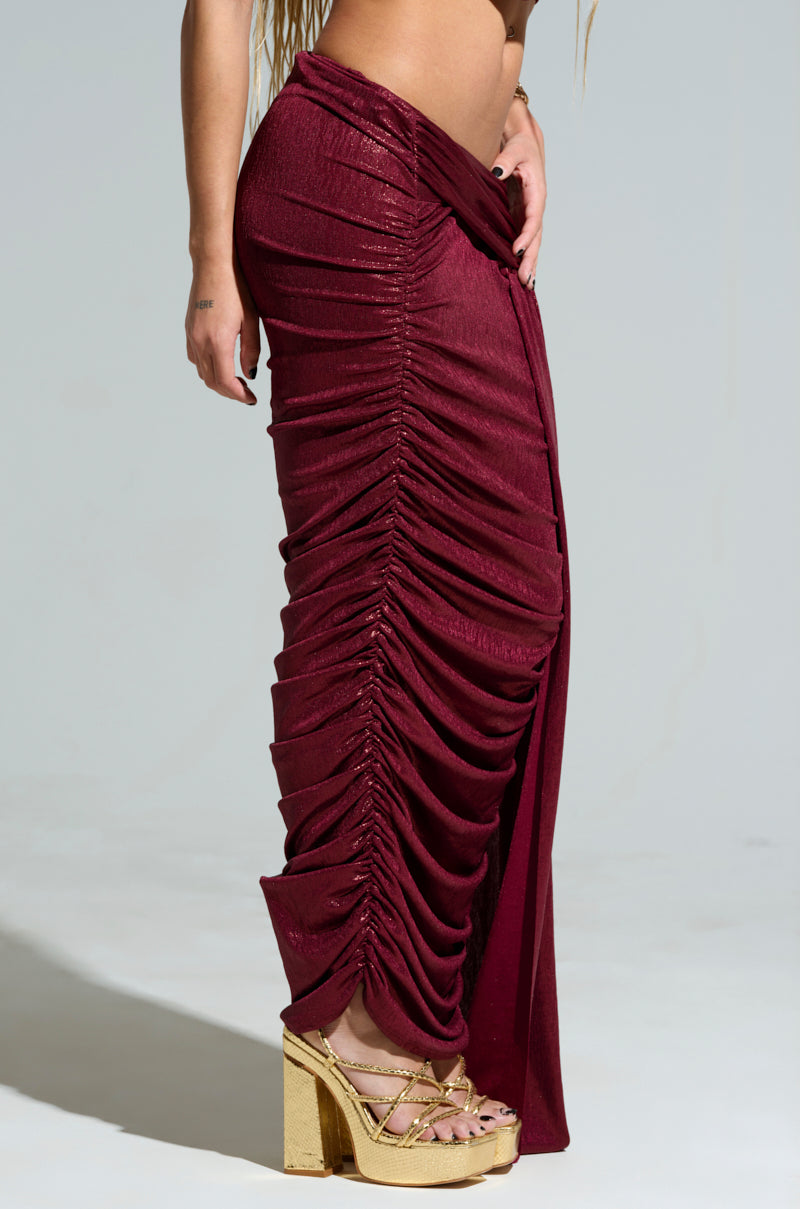 A person wearing the ALL OF THE GLAMOUR SLINKY MAXI SKIRT in a ruched, deep red design paired with gold platform sandals stands against a neutral background.