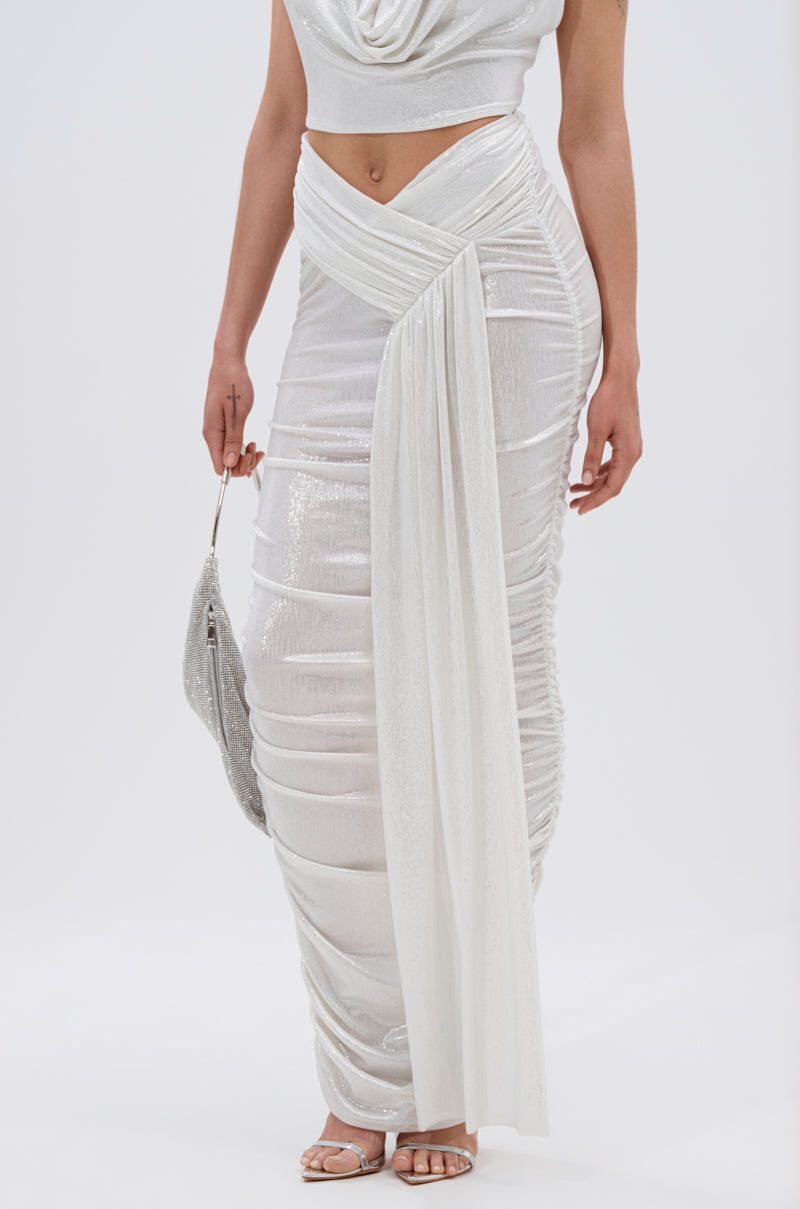 A model wears the ALL OF THE GLAMOUR SLINKY MAXI SKIRT IN WHITE featuring a high slit and V-line waist, paired with a matching sleeveless top, silver clutch, and strappy heels against a plain white background. 3