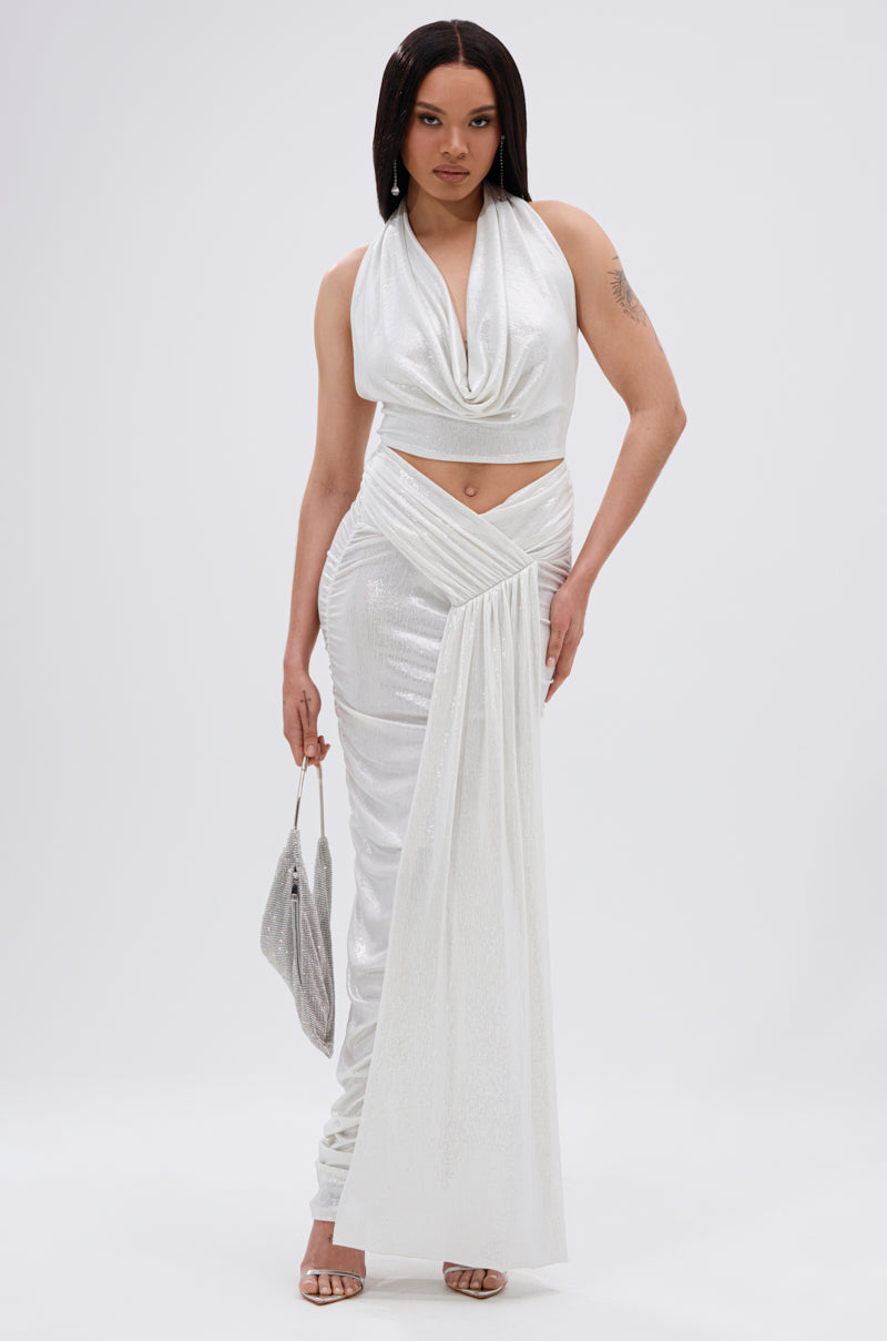 A woman in a shimmering white sleeveless top and the ALL OF THE GLAMOUR SLINKY MAXI SKIRT IN WHITE, featuring an asymmetrical V-line waist and ruched silhouette, holds a silver bag and wears heeled sandals against a plain white background. 9