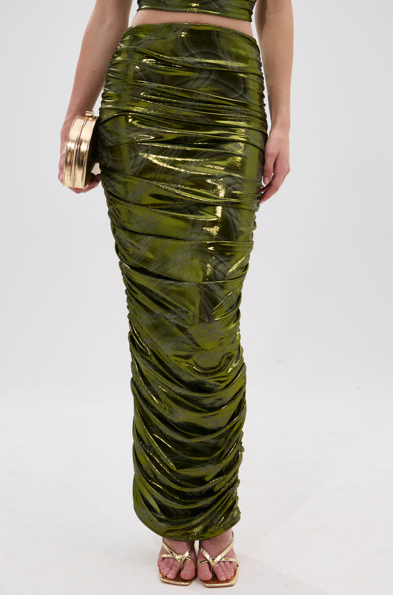 A person stands against a white background wearing the TAYLOR METALLIC RUCHED MAXI SKIRT in olive green with a matching top, accessorized with a gold clutch and strappy gold sandals. 1