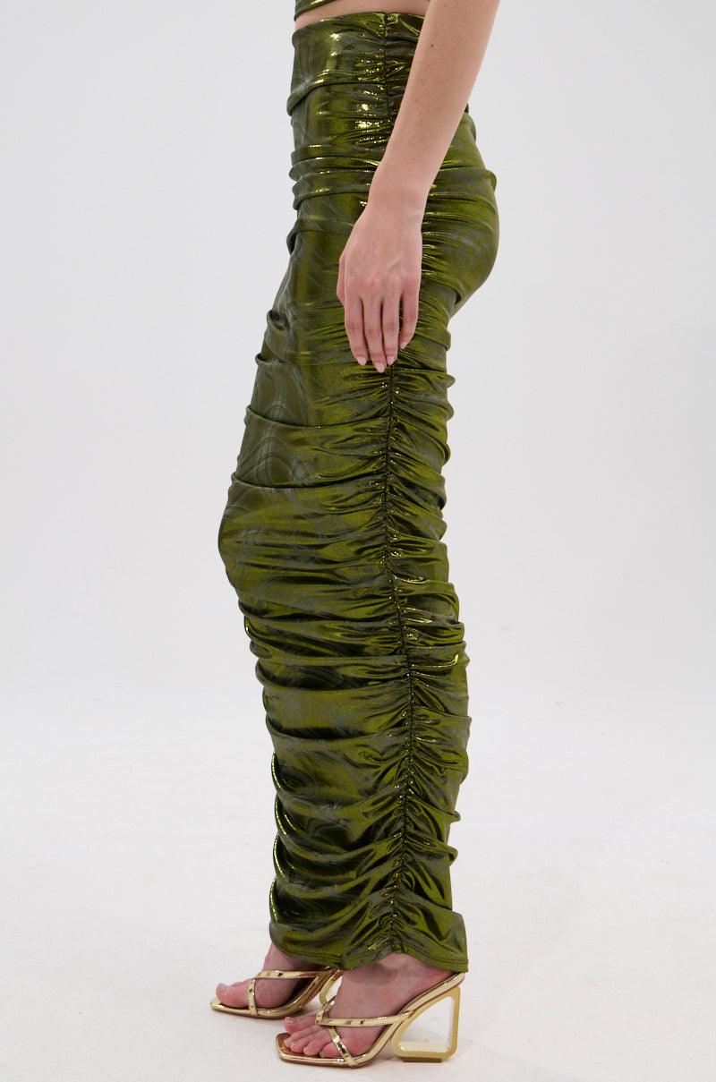 A person stands sideways against a white background, wearing the TAYLOR METALLIC RUCHED MAXI SKIRT in green with gold high-heeled sandals. 3