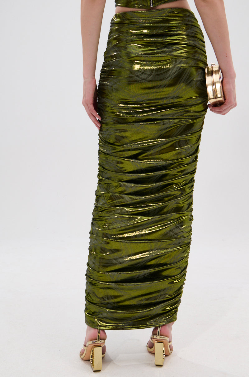 A person wears the TAYLOR METALLIC RUCHED MAXI SKIRT in green, paired with gold high-heeled sandals and a gold clutch. The image is cropped from the waist down against a plain light background. 4