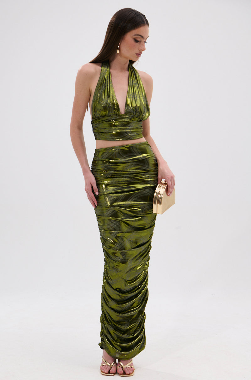 A woman stands against a white background wearing the TAYLOR METALLIC RUCHED MAXI SKIRT with a matching metallic green halter crop top, styled with gold heels, long earrings, and a gold clutch. 6