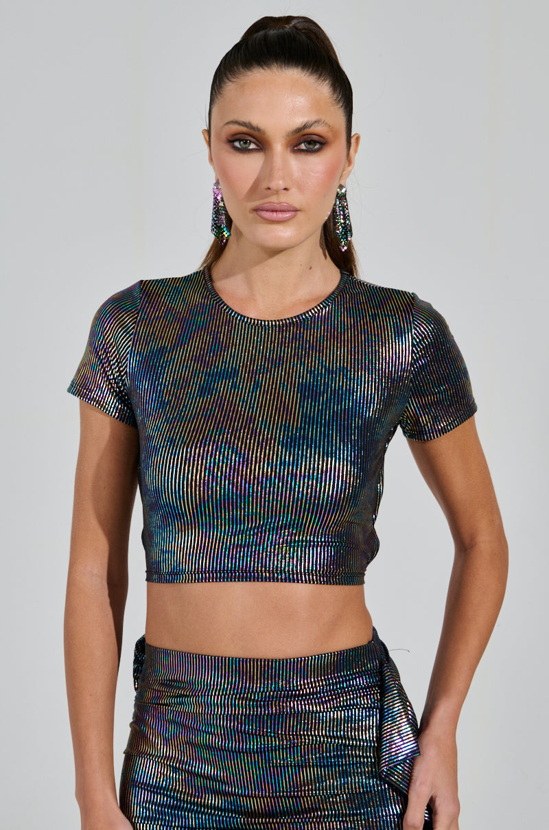 A person with long, sleek hair is wearing a shimmering ZEON TANK WITH TIE IN BACK and skirt featuring an iridescent striped pattern. They have matching earrings and are standing against a plain background.